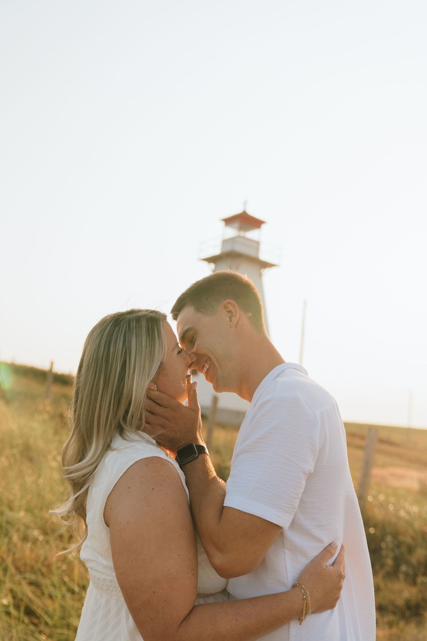 A romantic moment shared between two people in front of a lighthouse at golden hour.