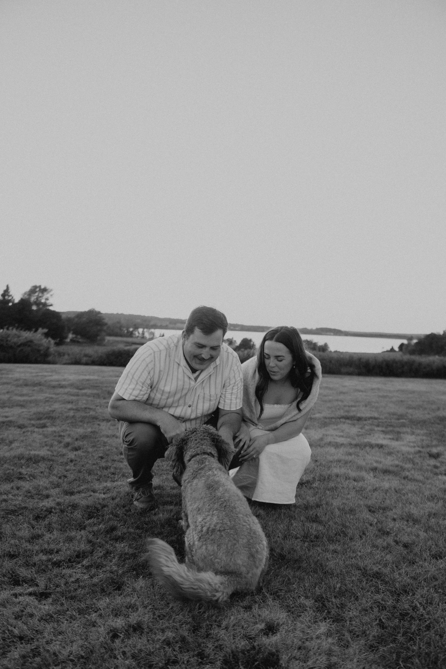 Couple playing with their dog in a grassy field at dusk.