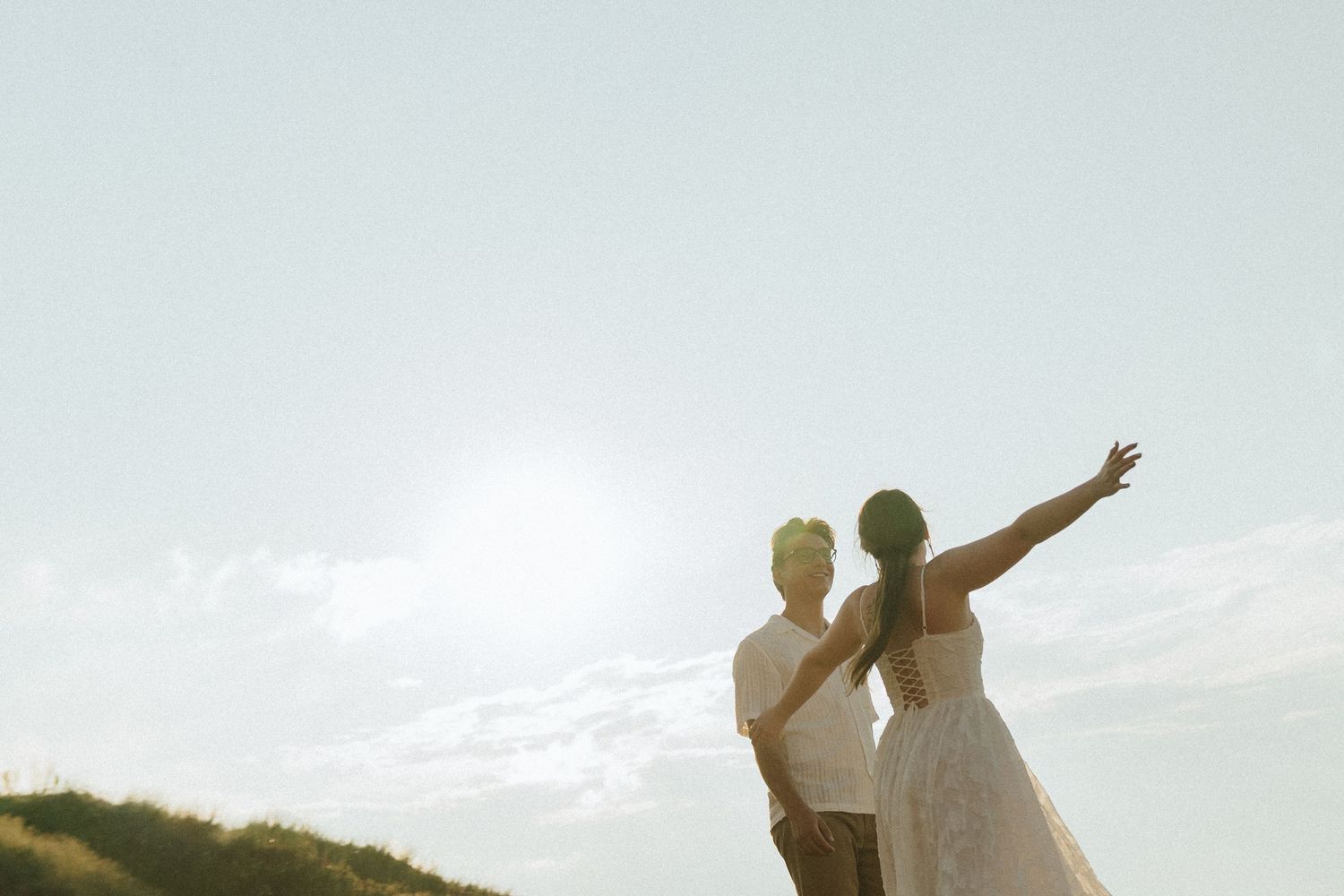 Silhouetted couple raises their arms joyfully against a bright sky during golden hour.