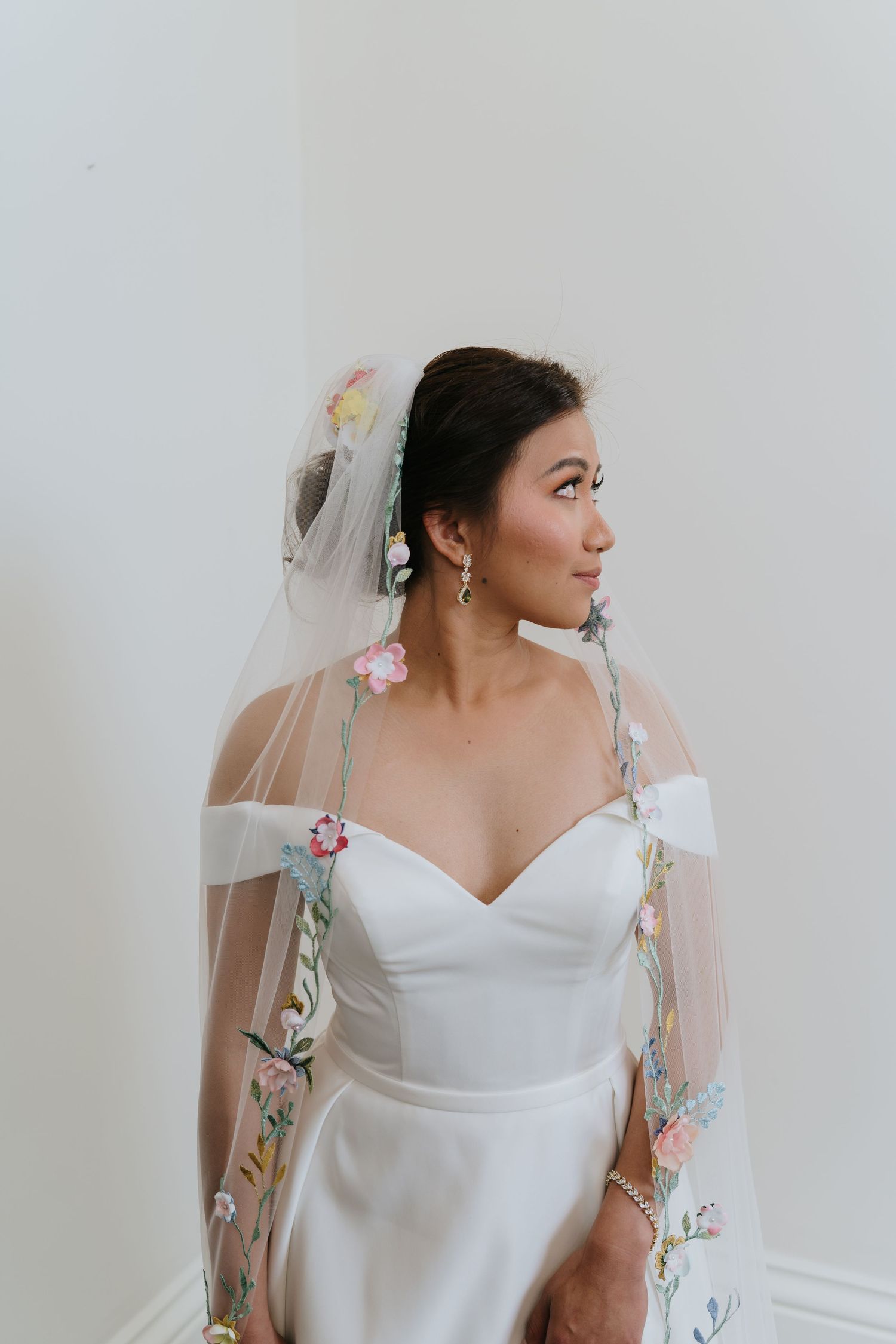 A bride in a white gown with sheer floral embellished sleeves poses against a light background.