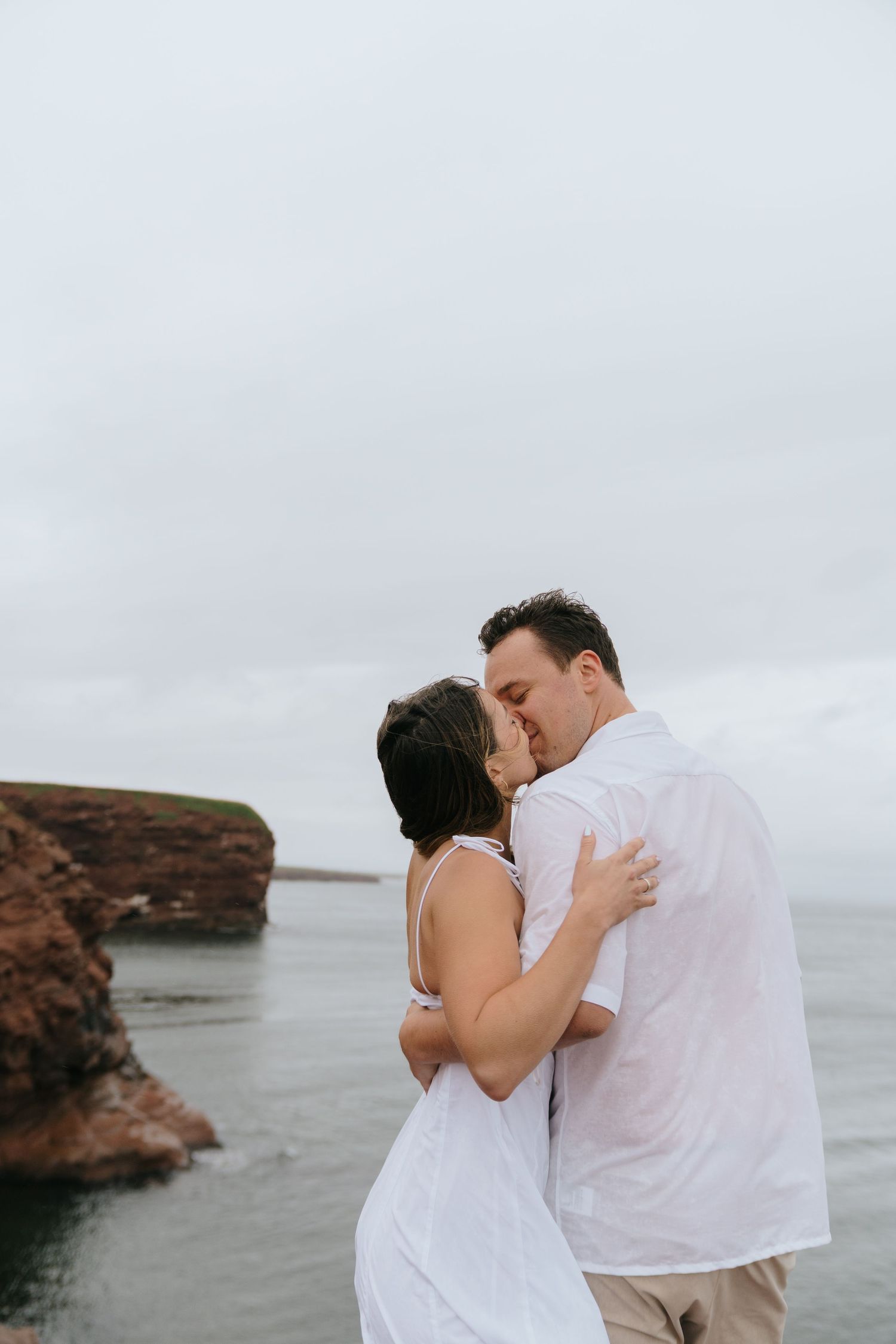Romantic couple embracing on a rocky coastline with dramatic cliffs in the background.