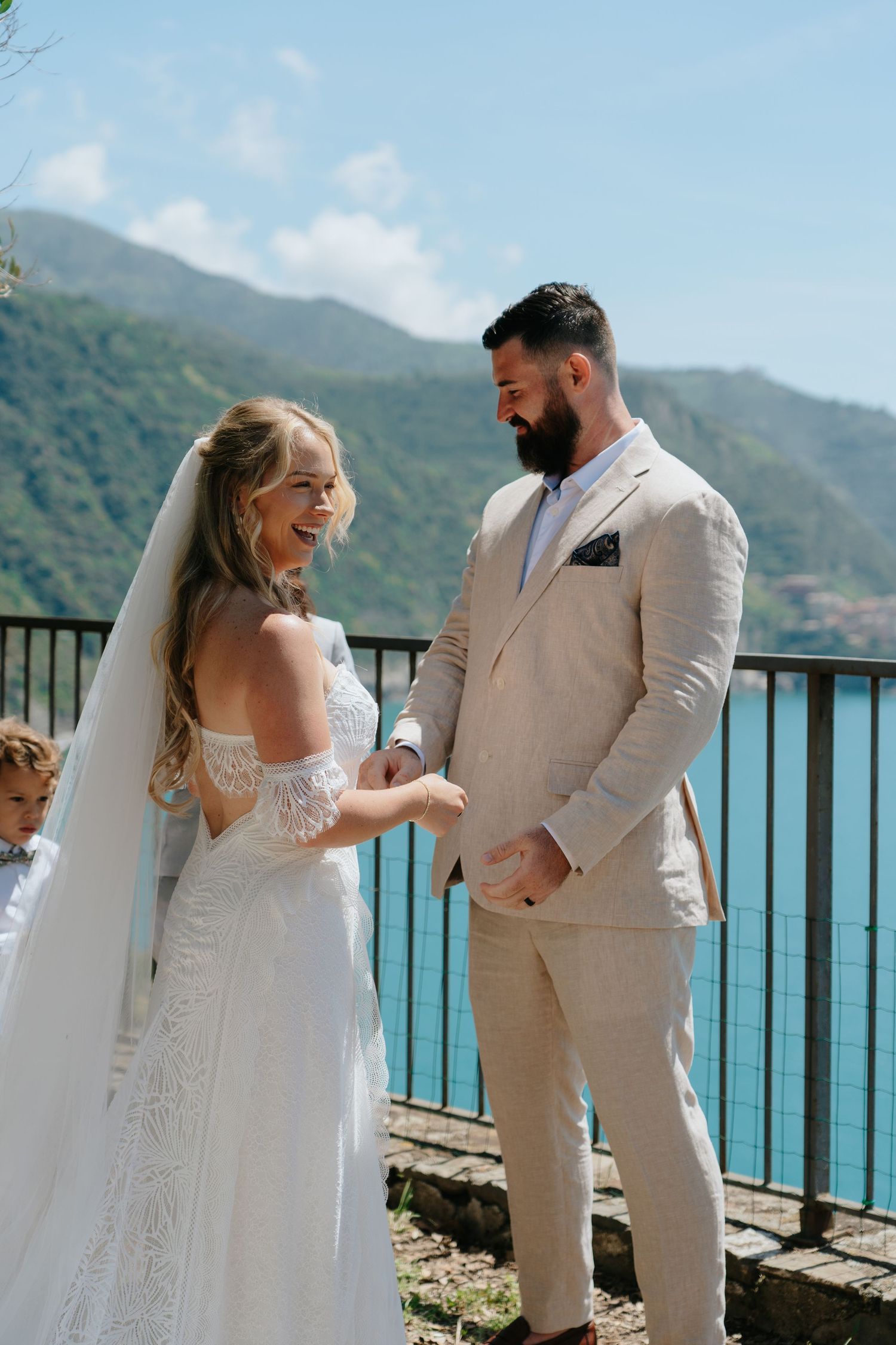 A couple shares an intimate moment during their wedding ceremony overlooking a stunning coastal mountain landscape.