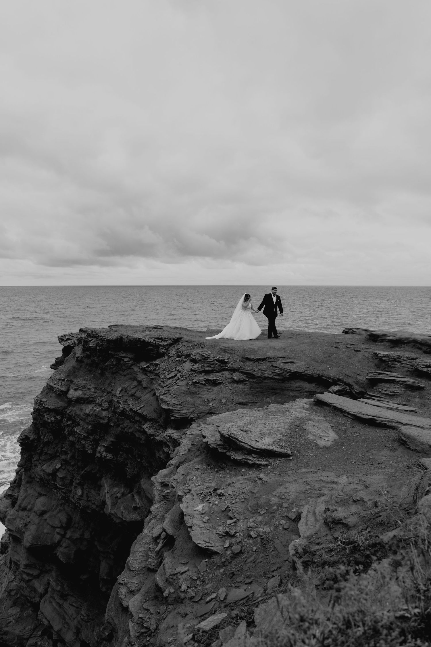 Wedding couple silhouetted against stormy skies on dramatic coastal cliffs.