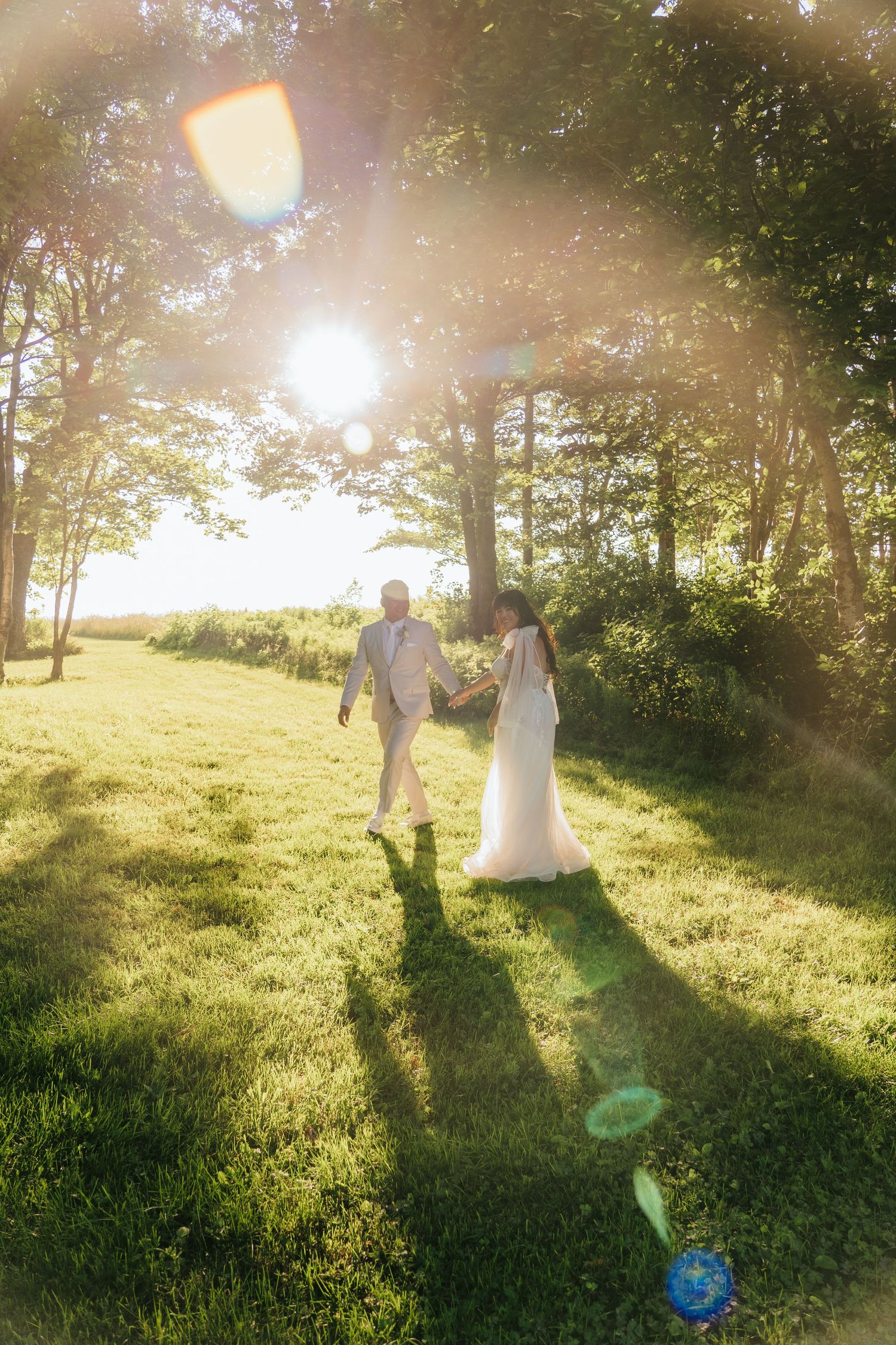 Wedding couple dances in a sunlit meadow surrounded by trees during golden hour.