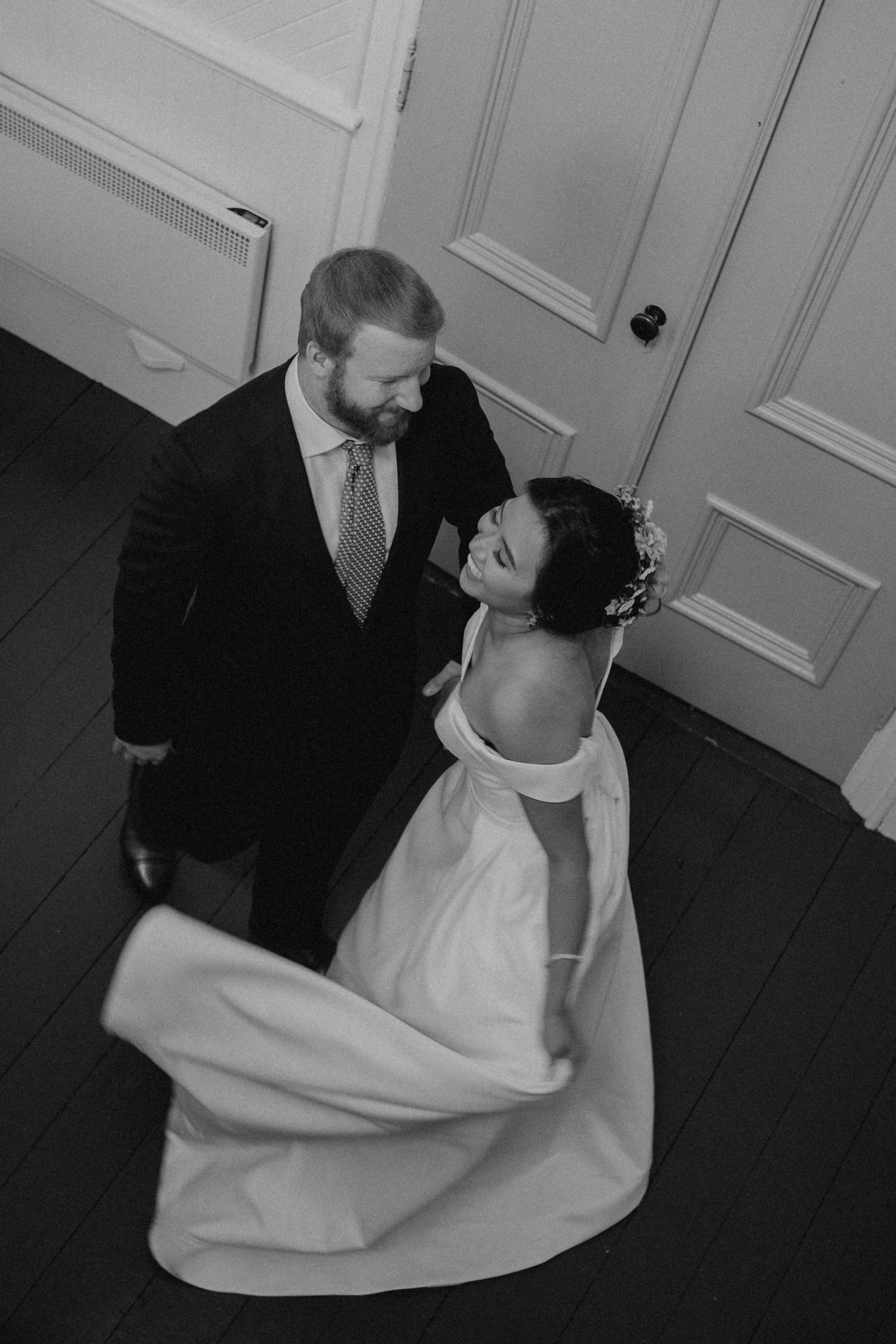 A couple shares an intimate dance moment in black and white on a dark wooden floor.