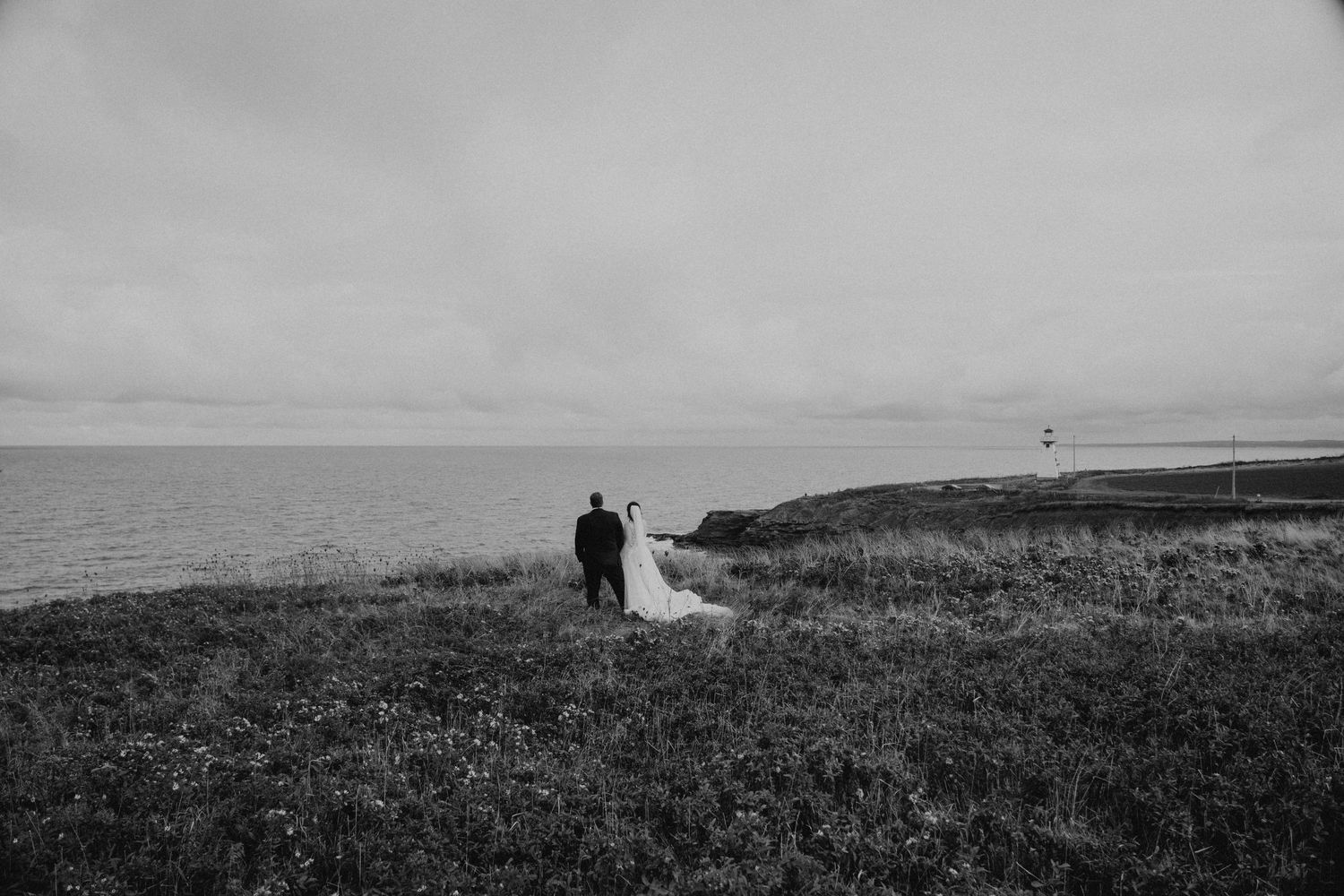 Distant silhouettes of a wedding couple walking along dramatic coastal cliffs.