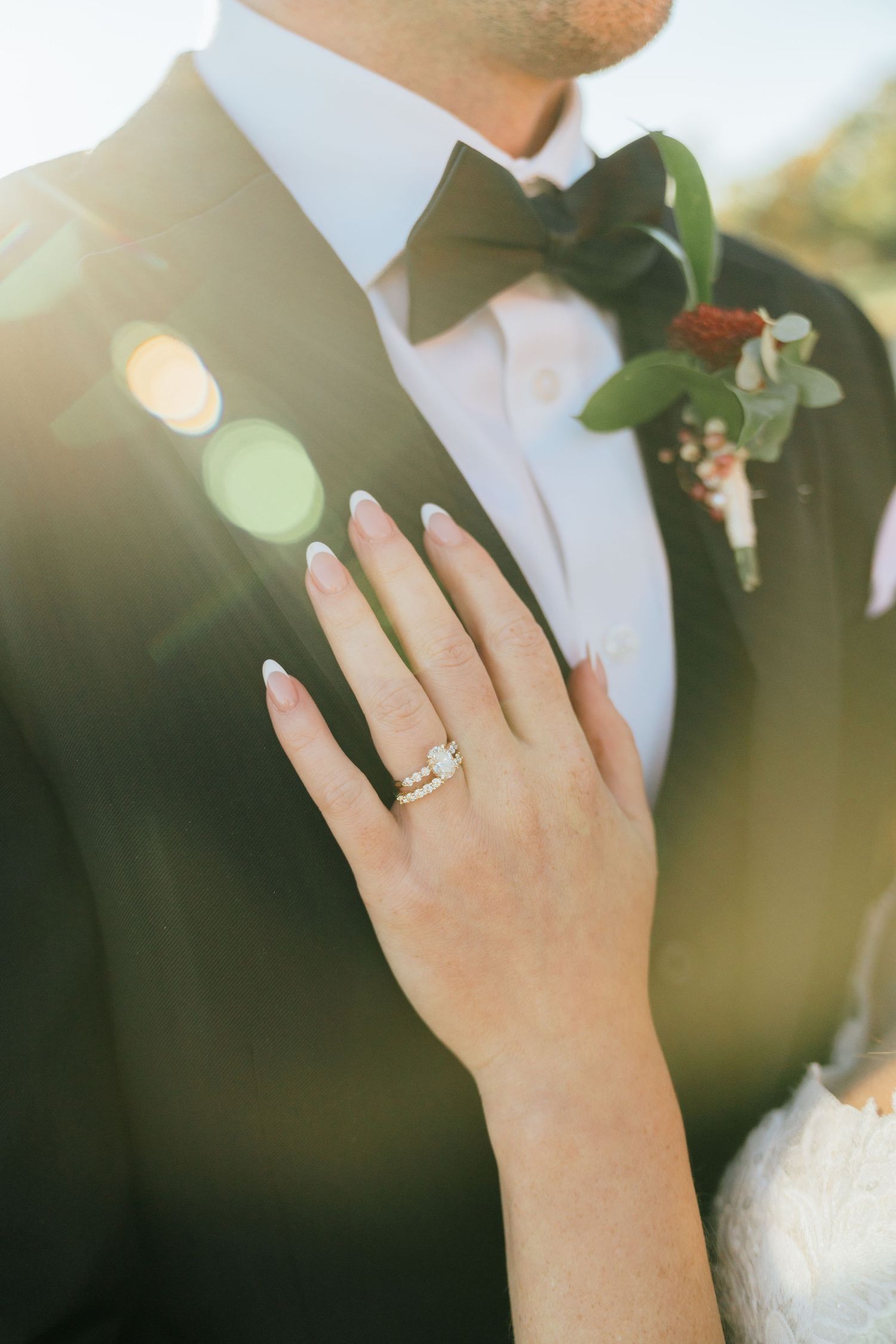 Close-up of a diamond ring and boutonniere on formal wedding attire in sunlit setting.