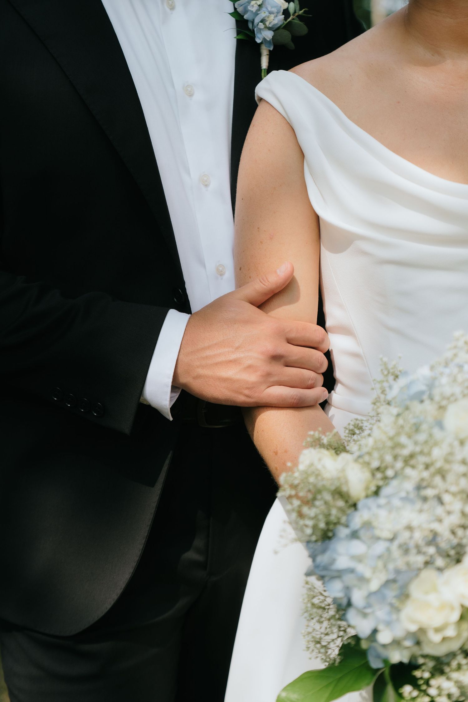 Close-up of bride and groom embracing, showing white dress and black tuxedo details.