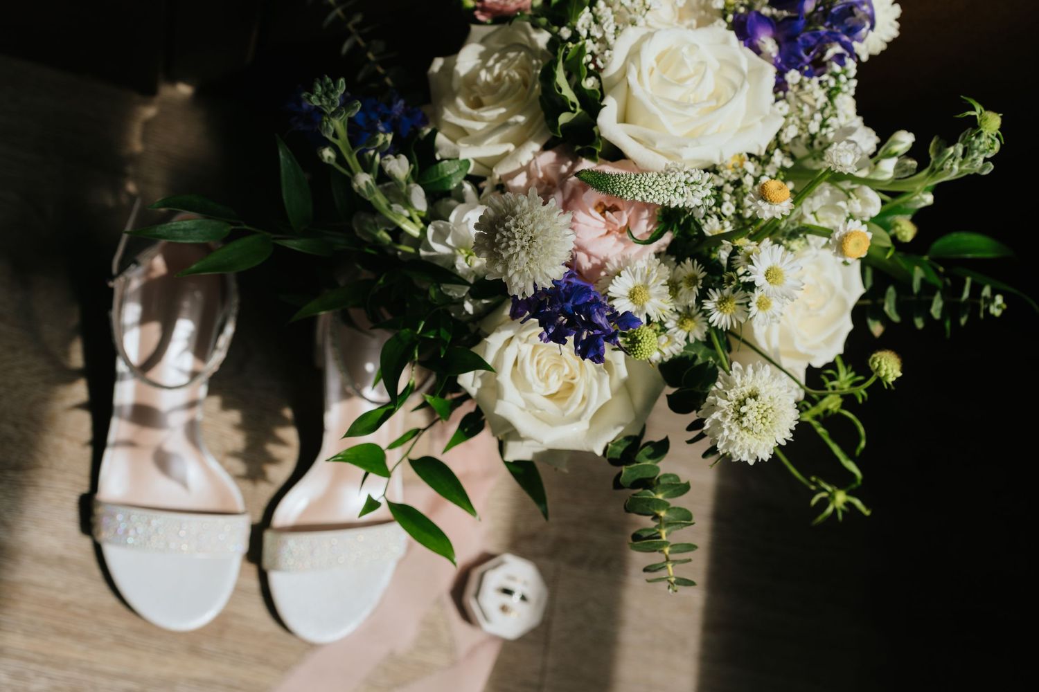 Elegant bridal bouquet with white roses and blue flowers next to wedding shoes.