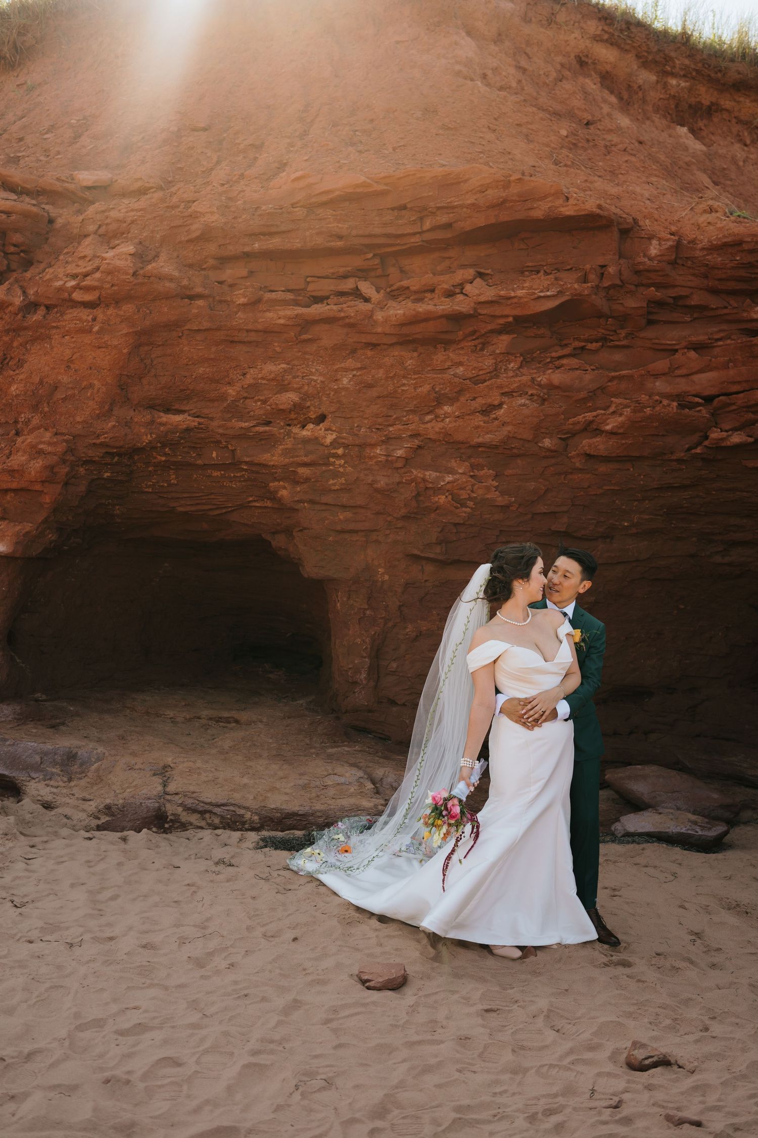 Romantic wedding portrait at sunset in front of a dramatic red rock cave formation.