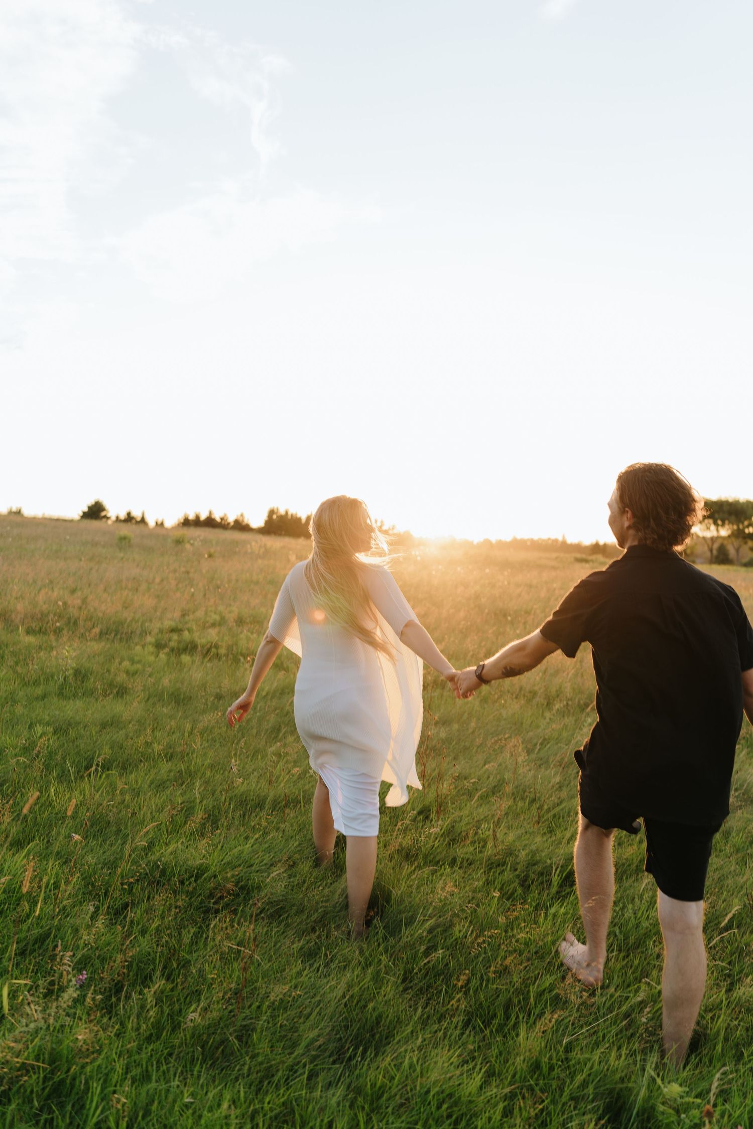 Couple running playfully through a sunlit meadow at sunset.