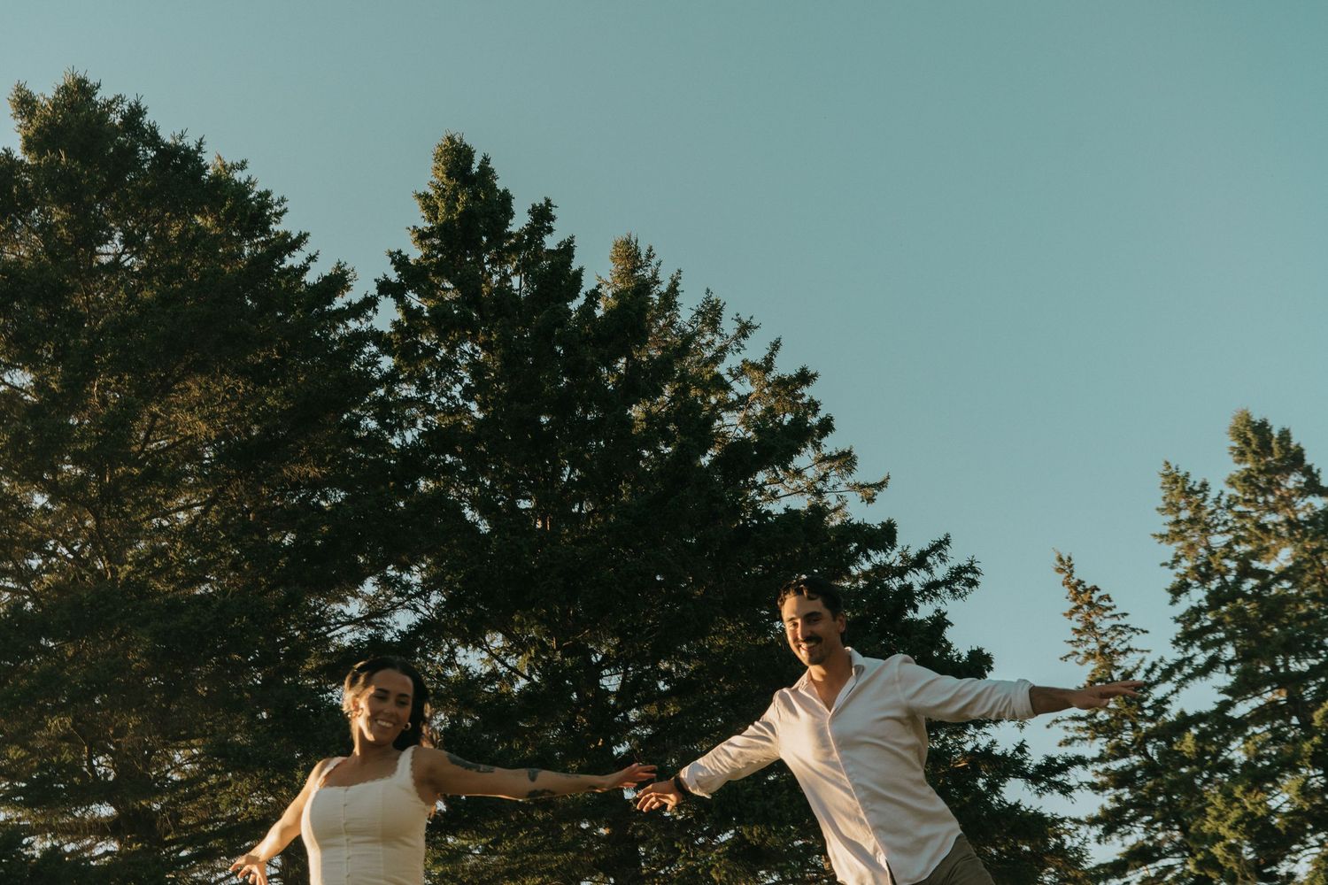 Joyful couple holding hands against pine trees during golden hour.