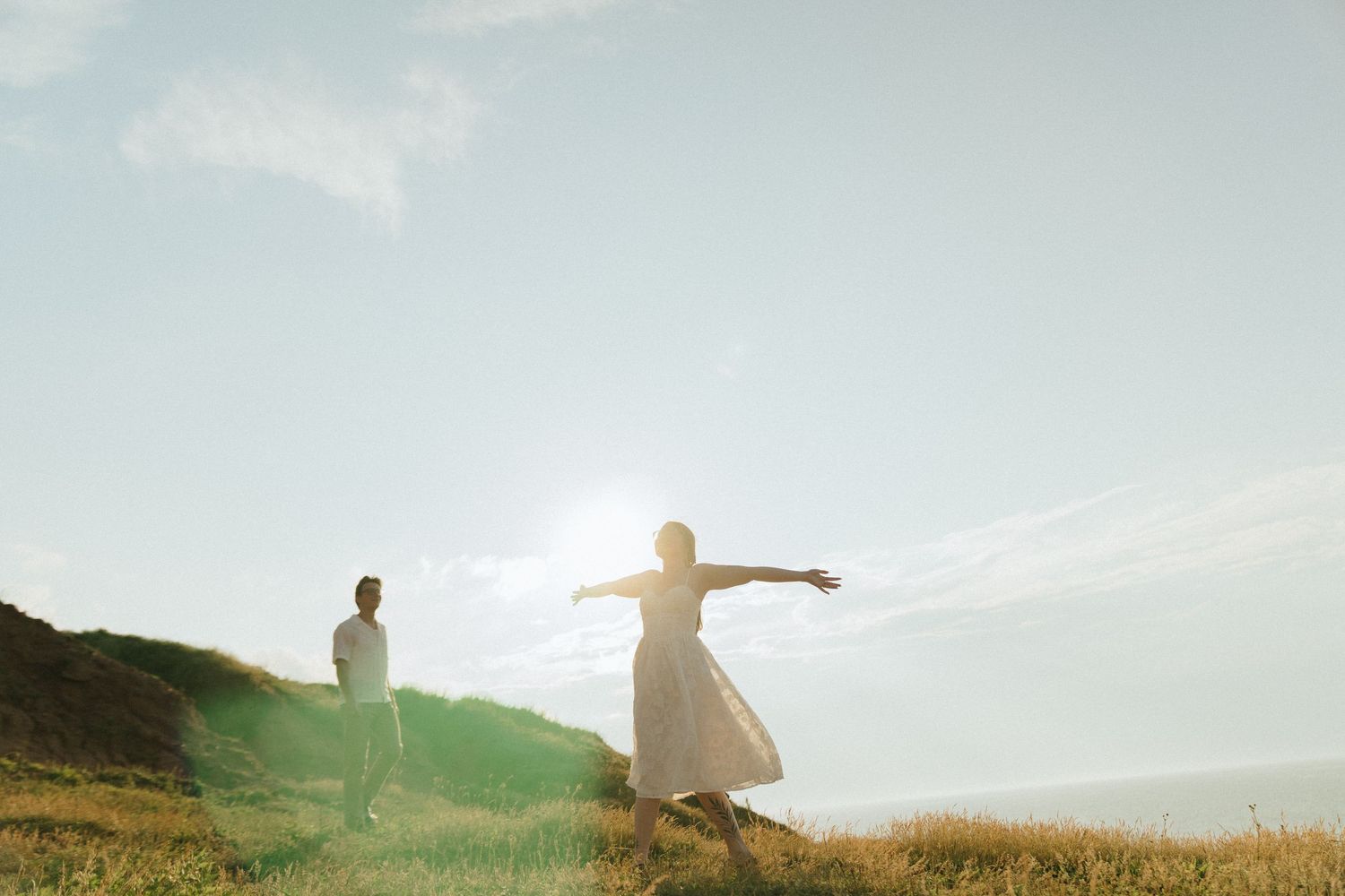 People stand in silhouette with arms outstretched against a bright sky in a grassy meadow at sunset.