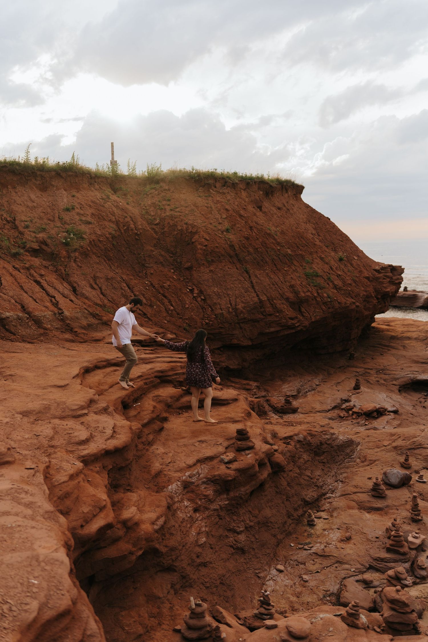 Two people explore the rugged red sandstone cliffs along a rocky beach during sunset at Thunder Cove, PEI.