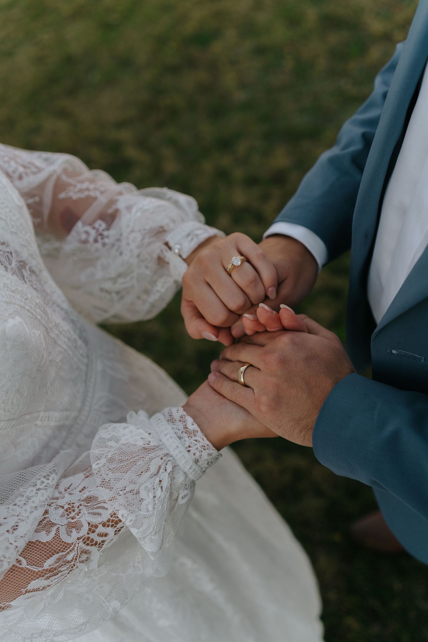Close-up of couple's hands with wedding rings against lace dress detail.