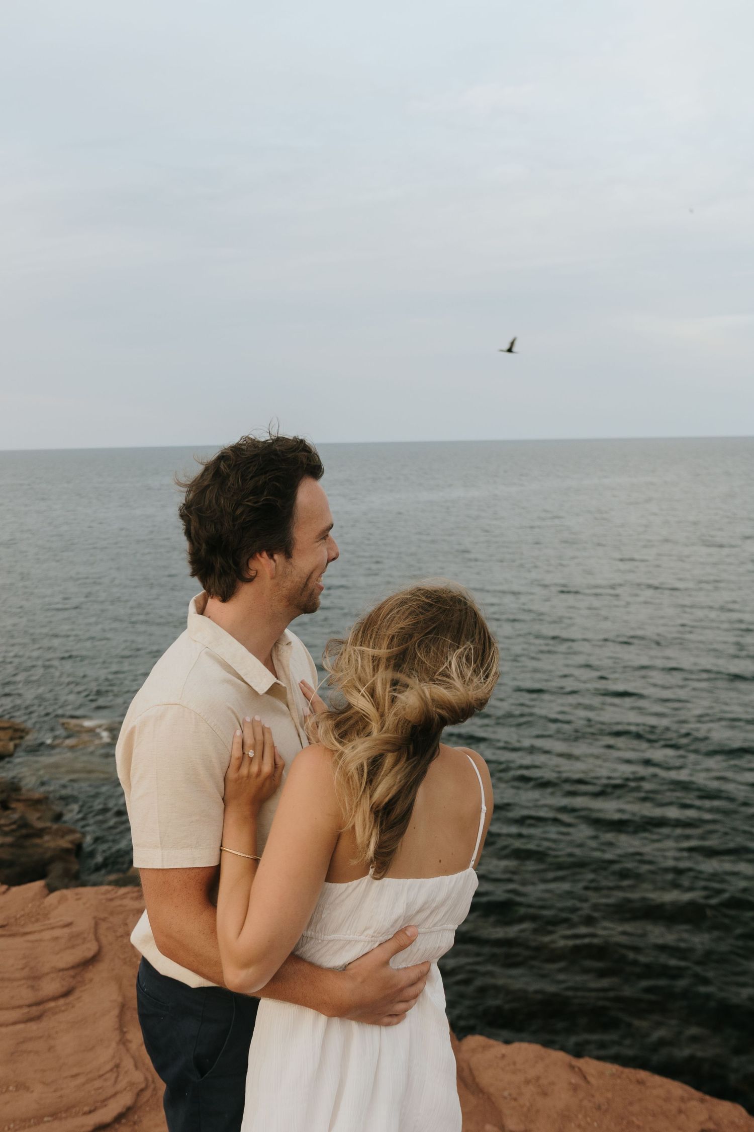 Romantic embrace on coastal cliffs with ocean view at sunset.