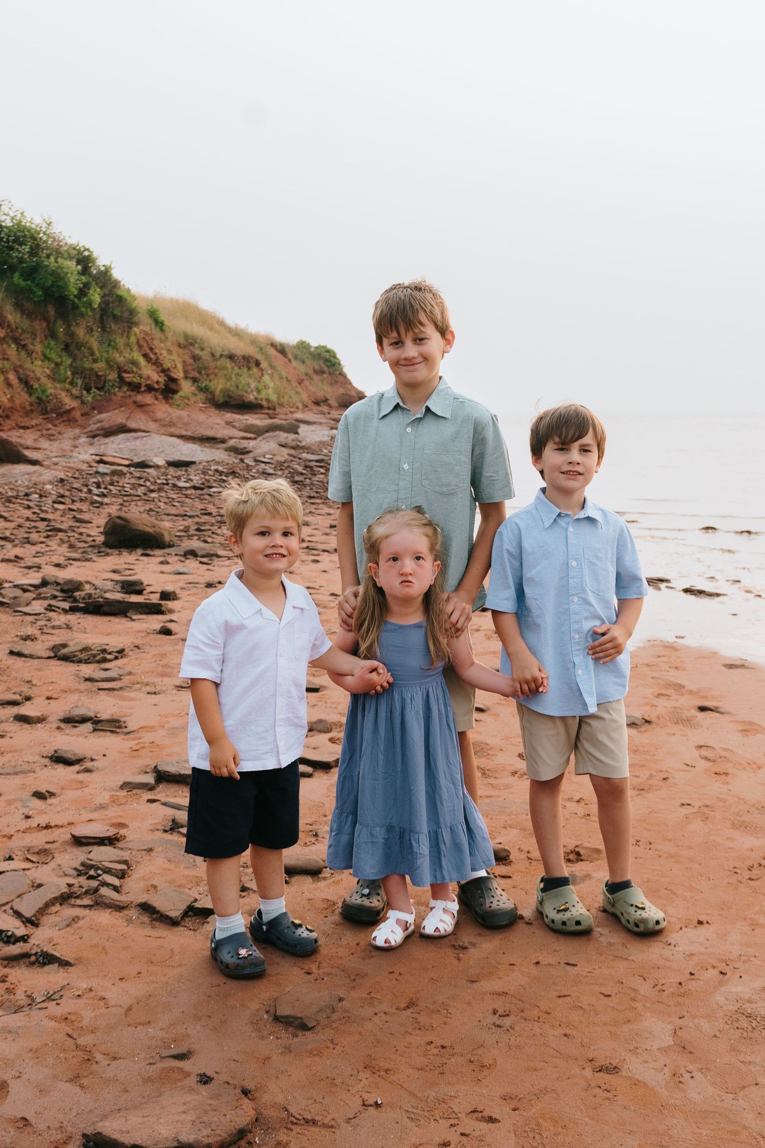 Children in coordinating blue and white outfits standing on red rocks at the beach.