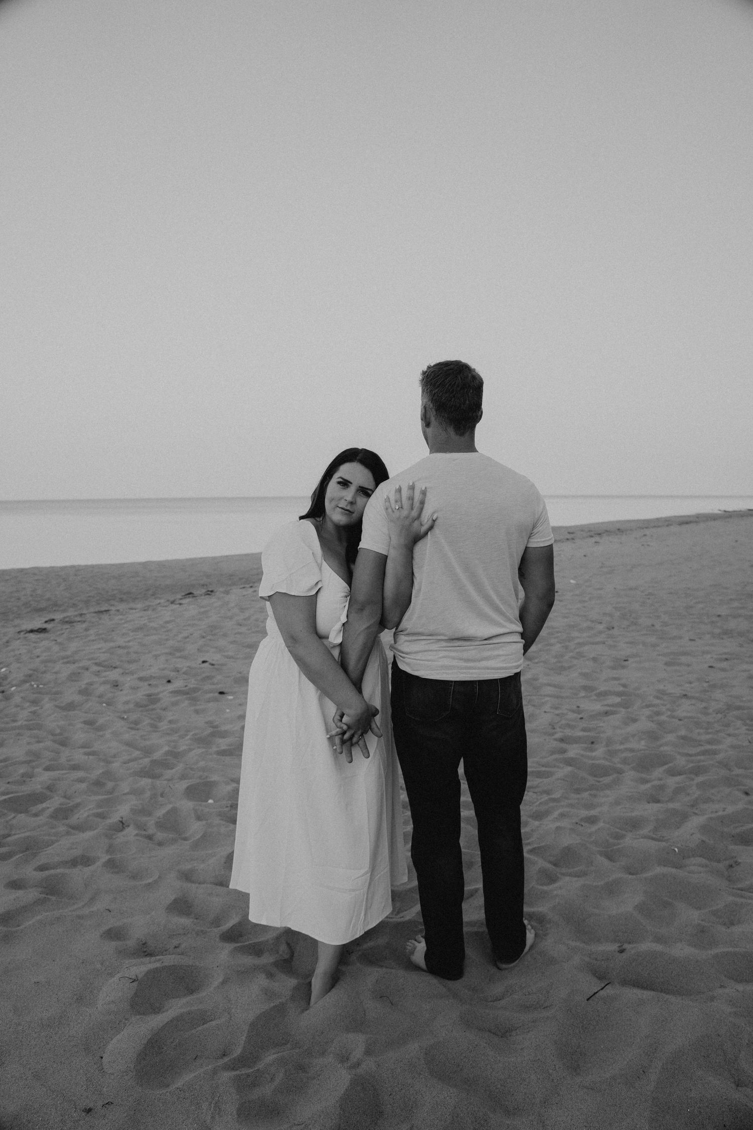 Black and white photo of couple walking intimately on a sandy beach.