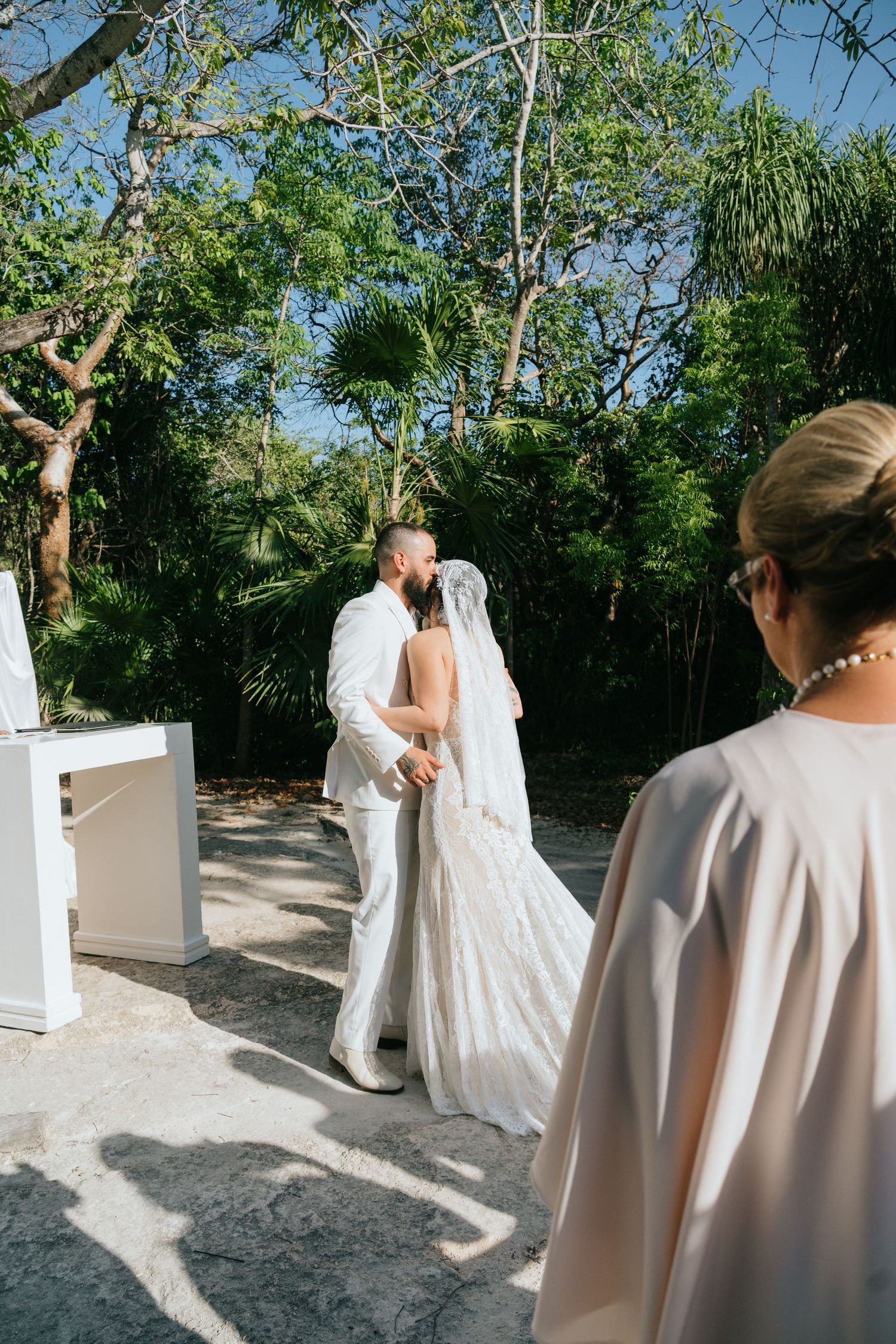 Bride and groom share a first kiss at an outdoor wedding ceremony surrounded by lush tropical greenery.