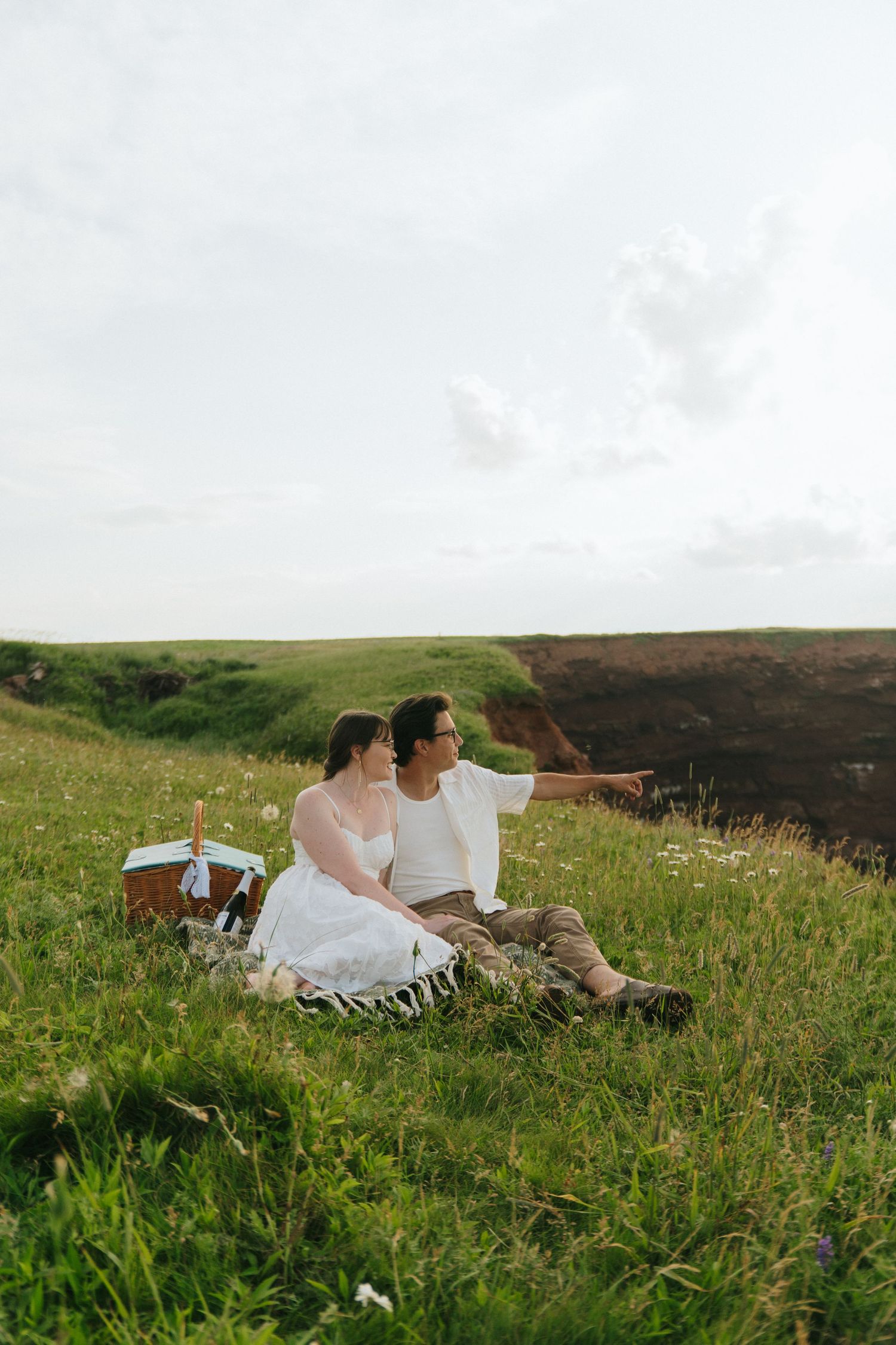 A couple relaxes together in a scenic meadow filled with wildflowers and rolling hills in the background.