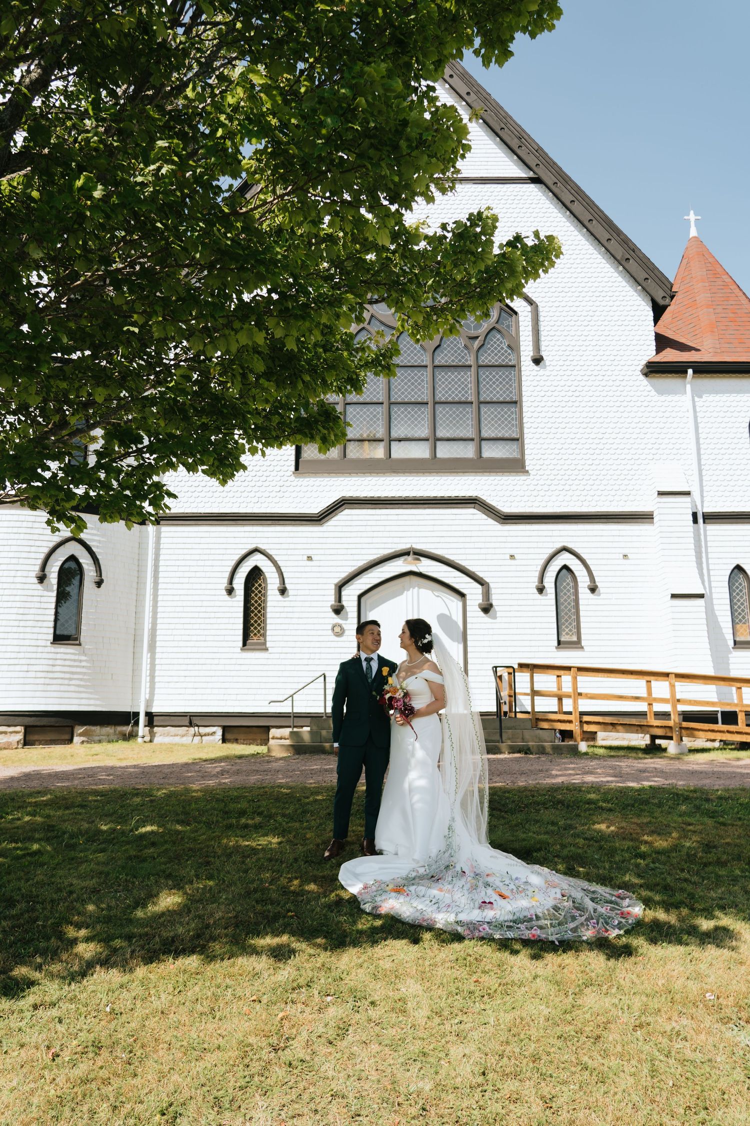 Wedding couple poses in front of a classic white church with Gothic architecture.