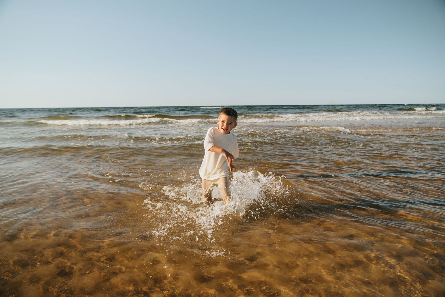 Person splashing through shallow ocean waves at the beach.