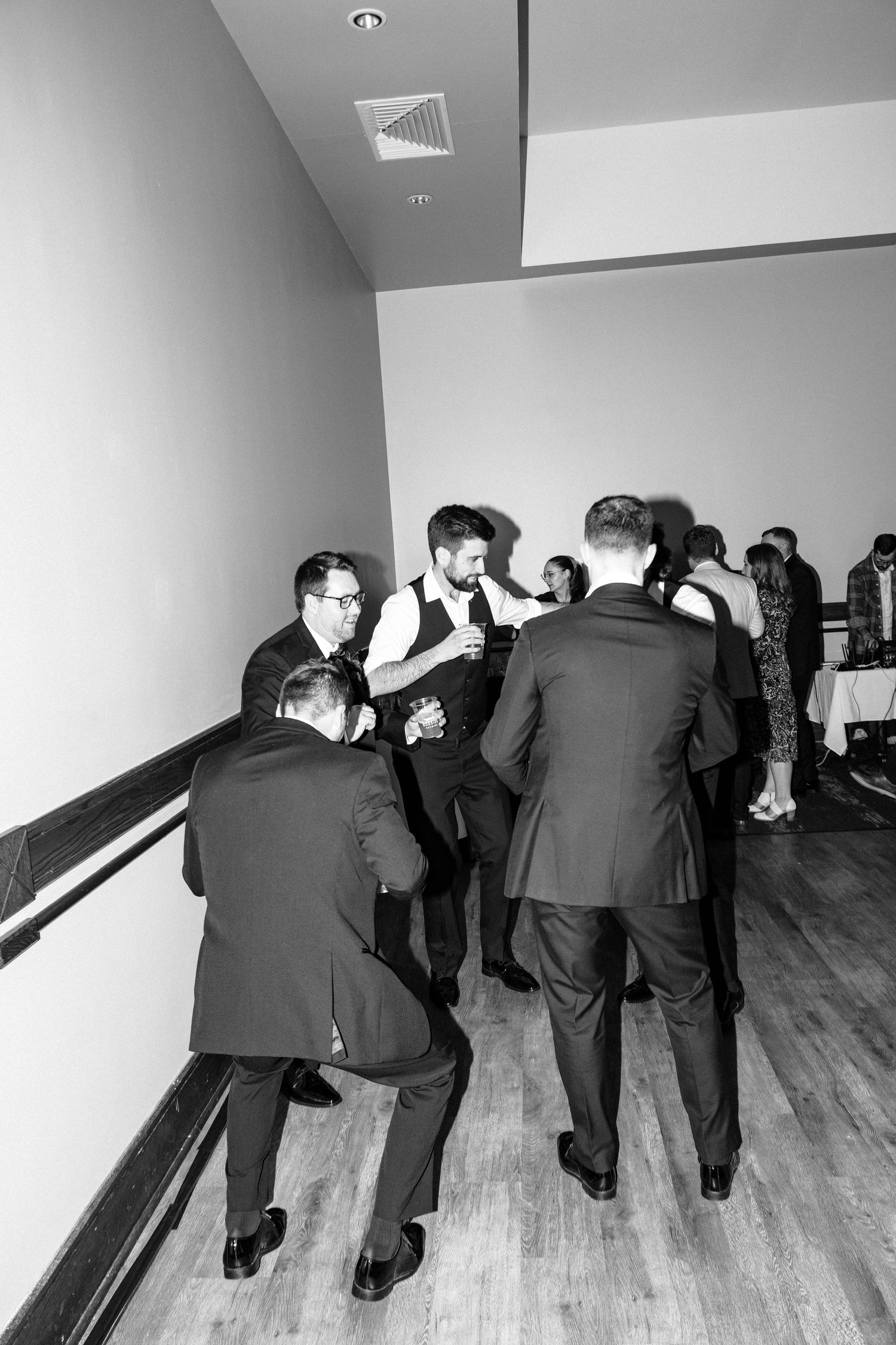 Black and white photo of groomsmen in suits gathered together laughing and celebrating at a wedding reception.