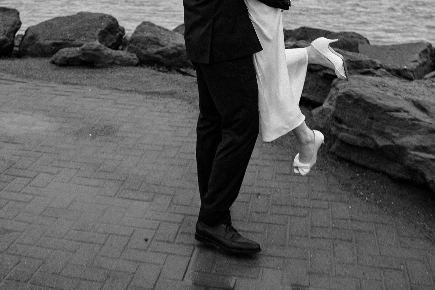 Couple walking along rocky coastal shoreline during a wedding photo session.