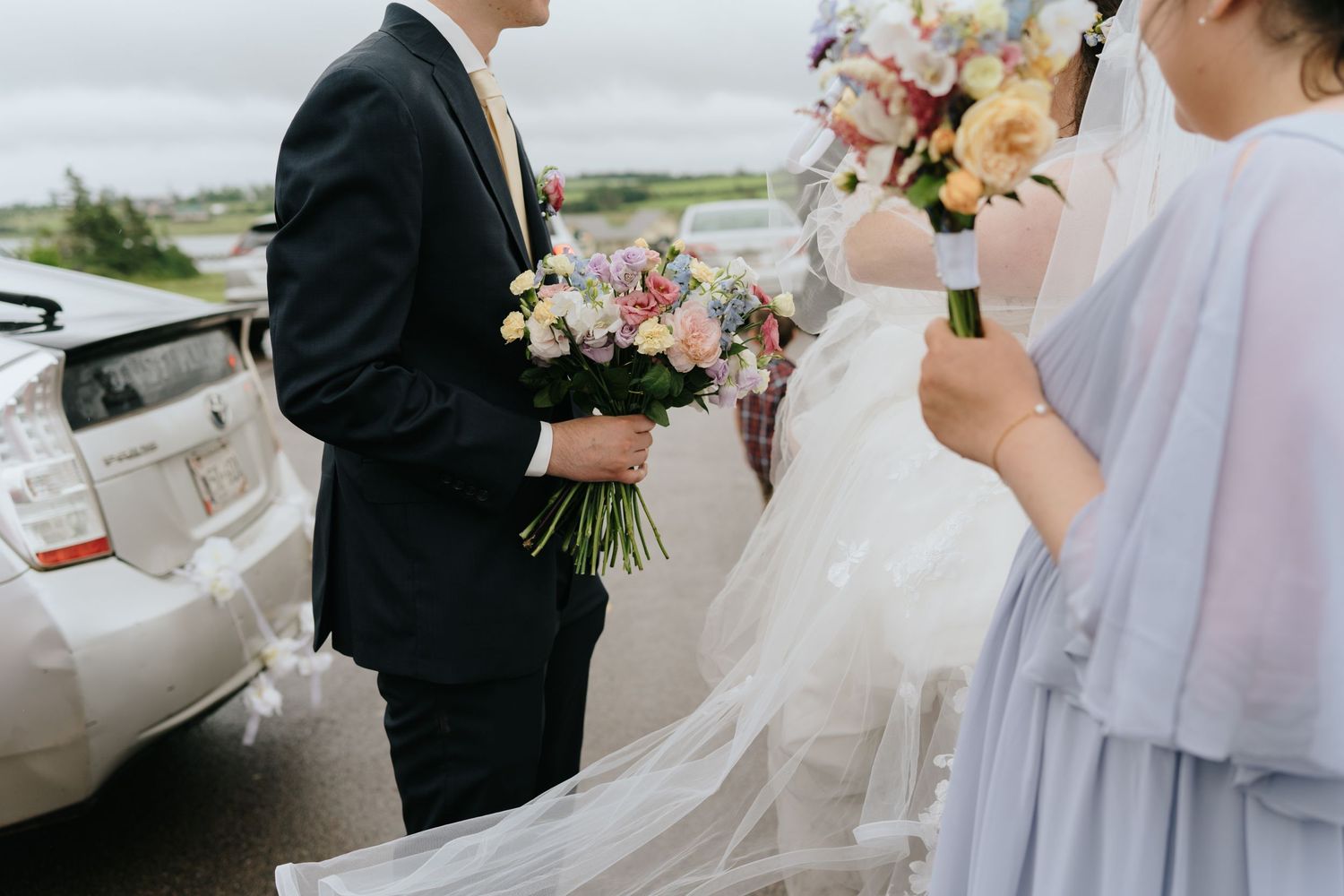 Wedding party members in white and light colored attire holding floral bouquets.