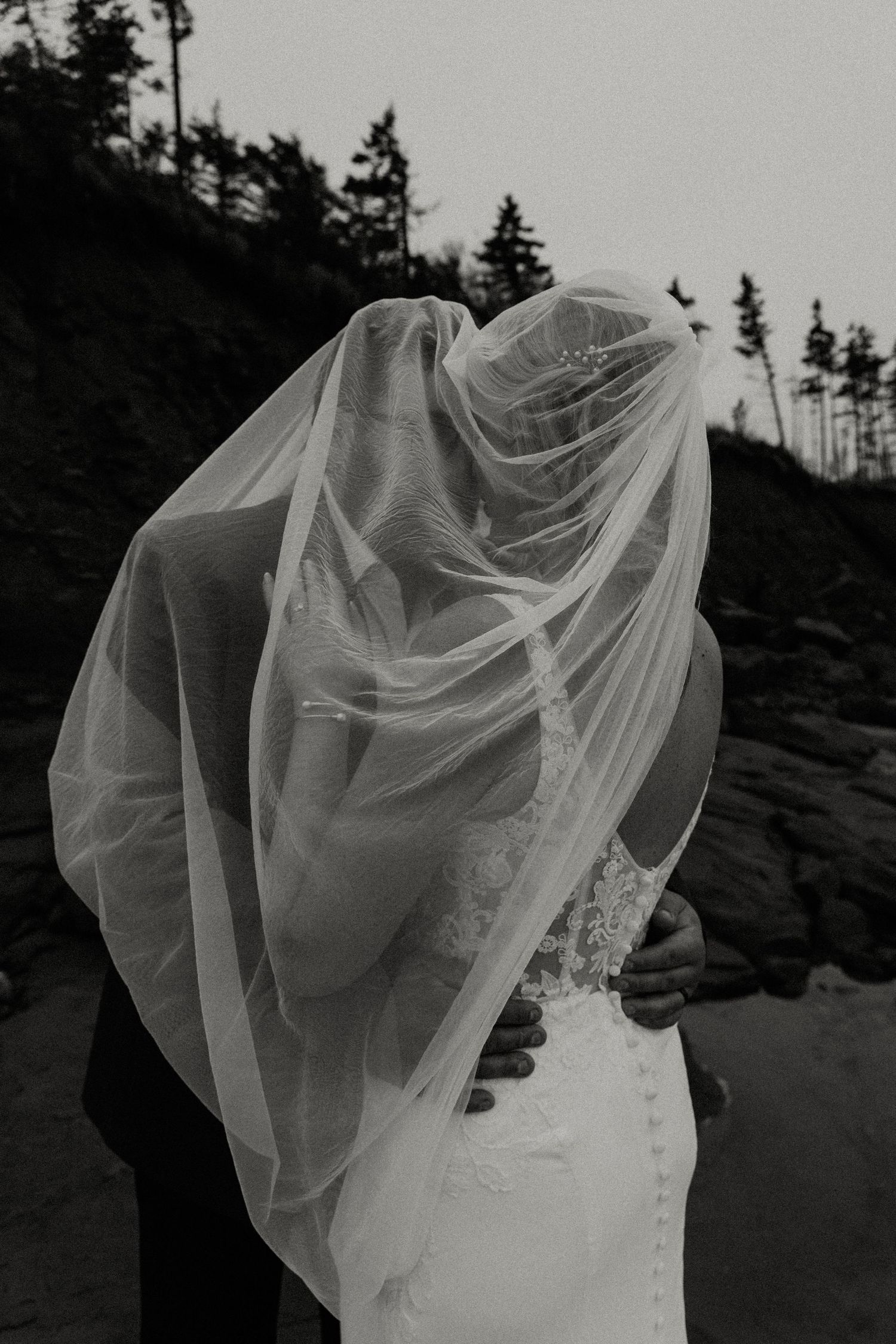 Dramatic black and white photo of a bride's veil flowing in the wind against a mountainous backdrop.