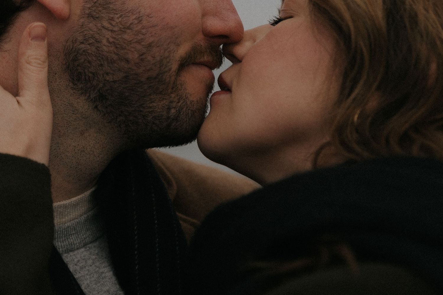 Intimate close-up of a couple sharing a tender kiss in moody lighting.