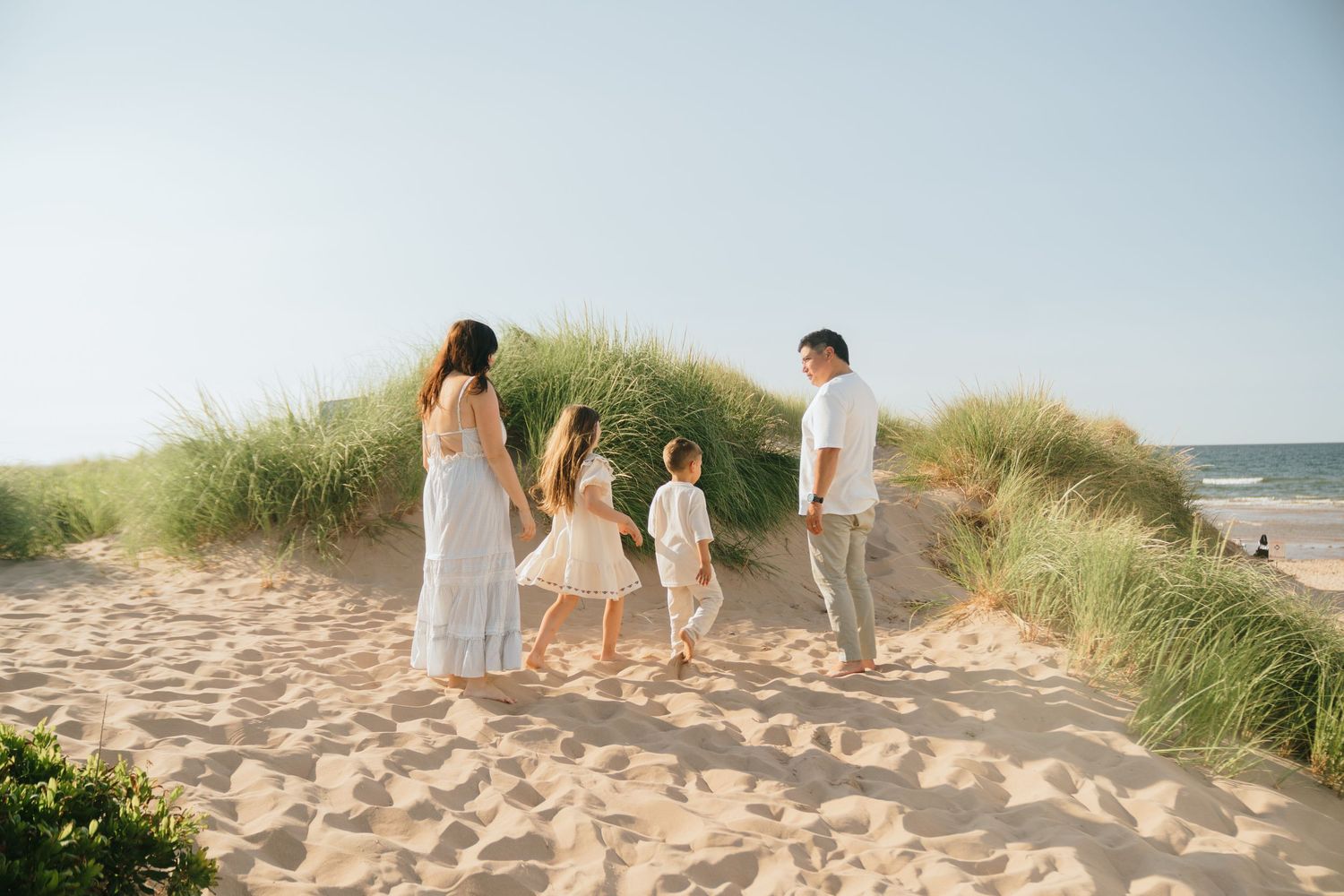A family walks together on sandy beach dunes during a sunny day.