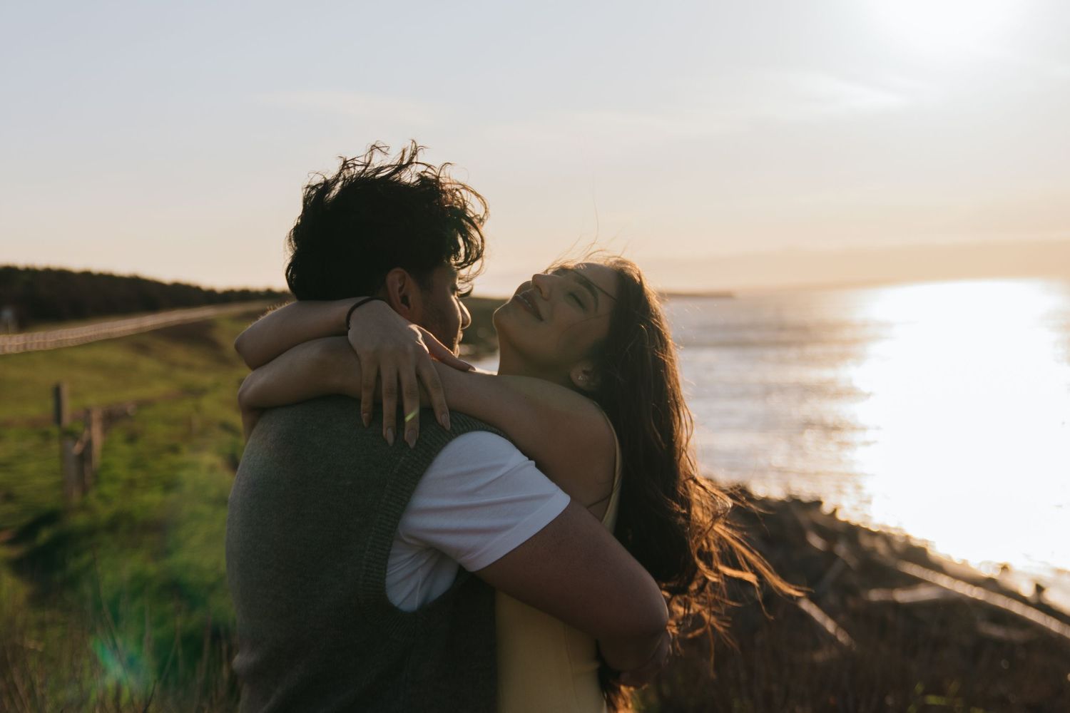 Couple embraces while watching golden sunset over coastal cliffs and ocean waves.
