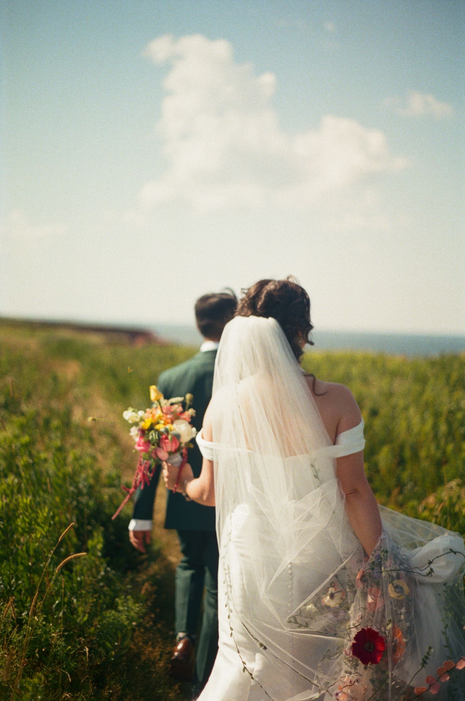 Couple in wedding attire sitting together in a sunny meadow with wildflowers.