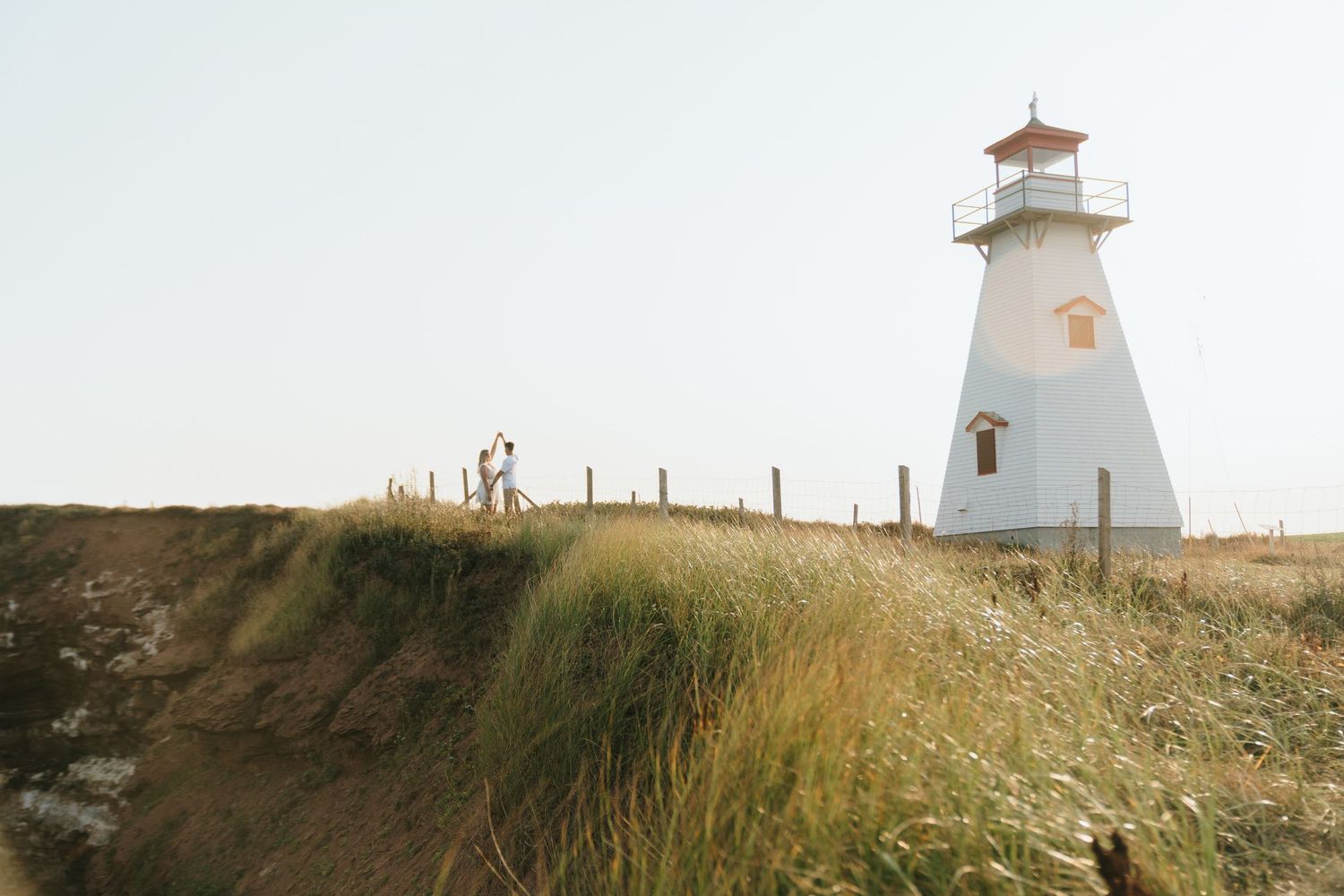 White lighthouse stands tall on grassy coastal cliff against cloudy sky at Prince Edward Island.