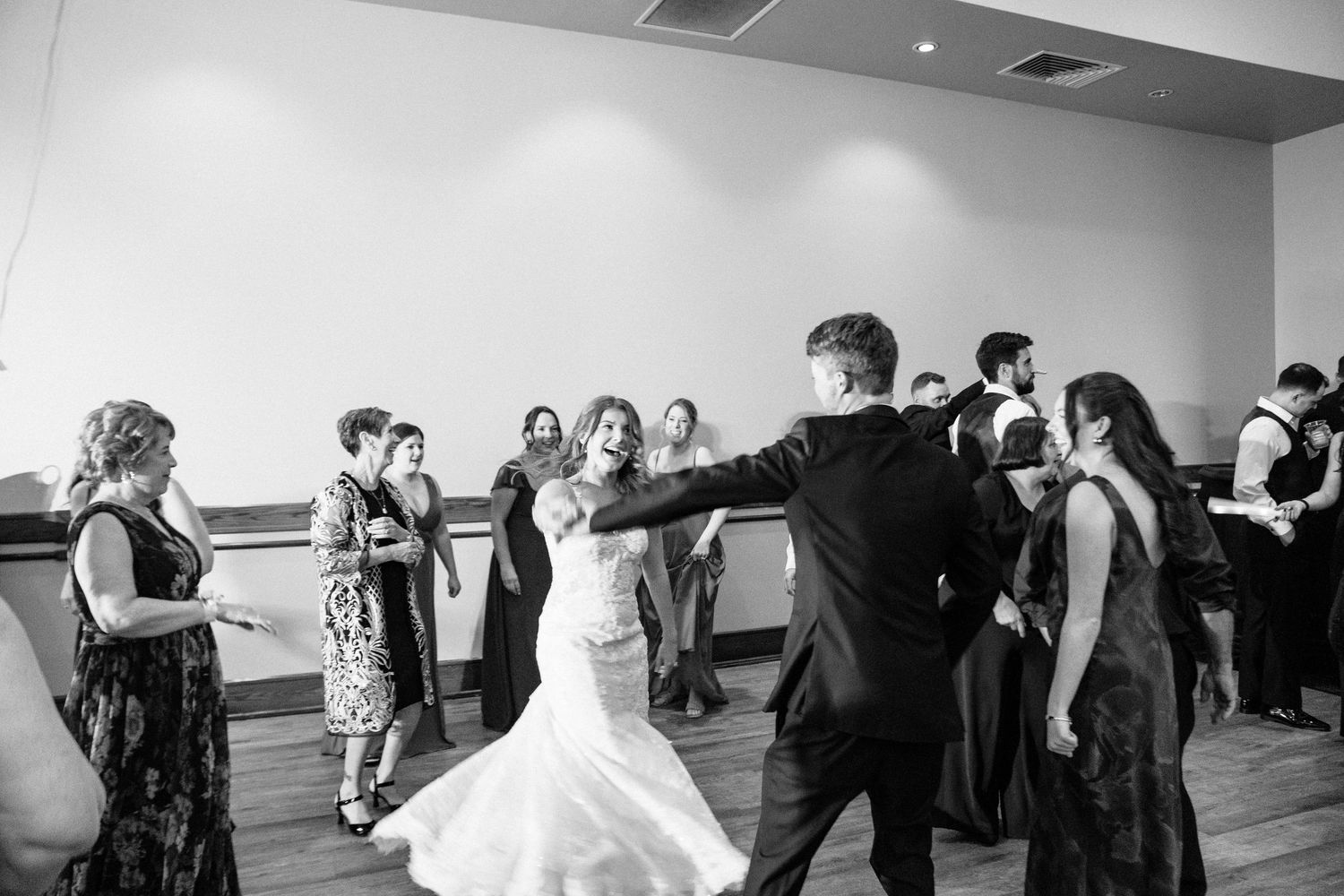 Bride and groom share a dance with guests at a wedding reception in black and white photo.
