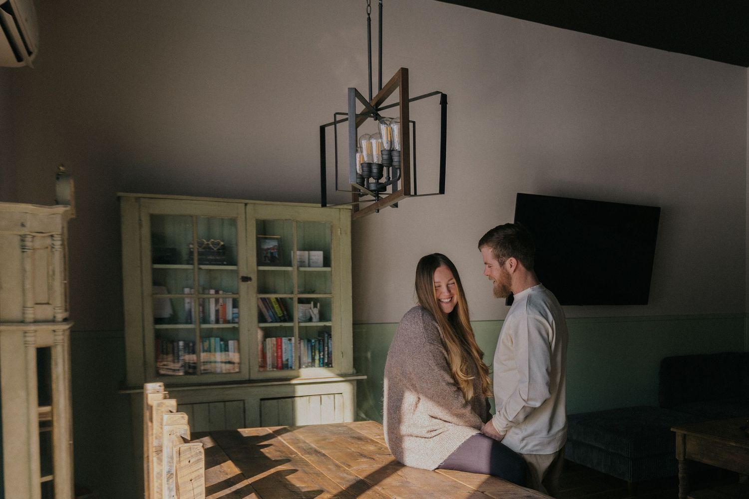 Couple sharing an intimate moment in a cozy home interior with bookshelves and pendant lighting.