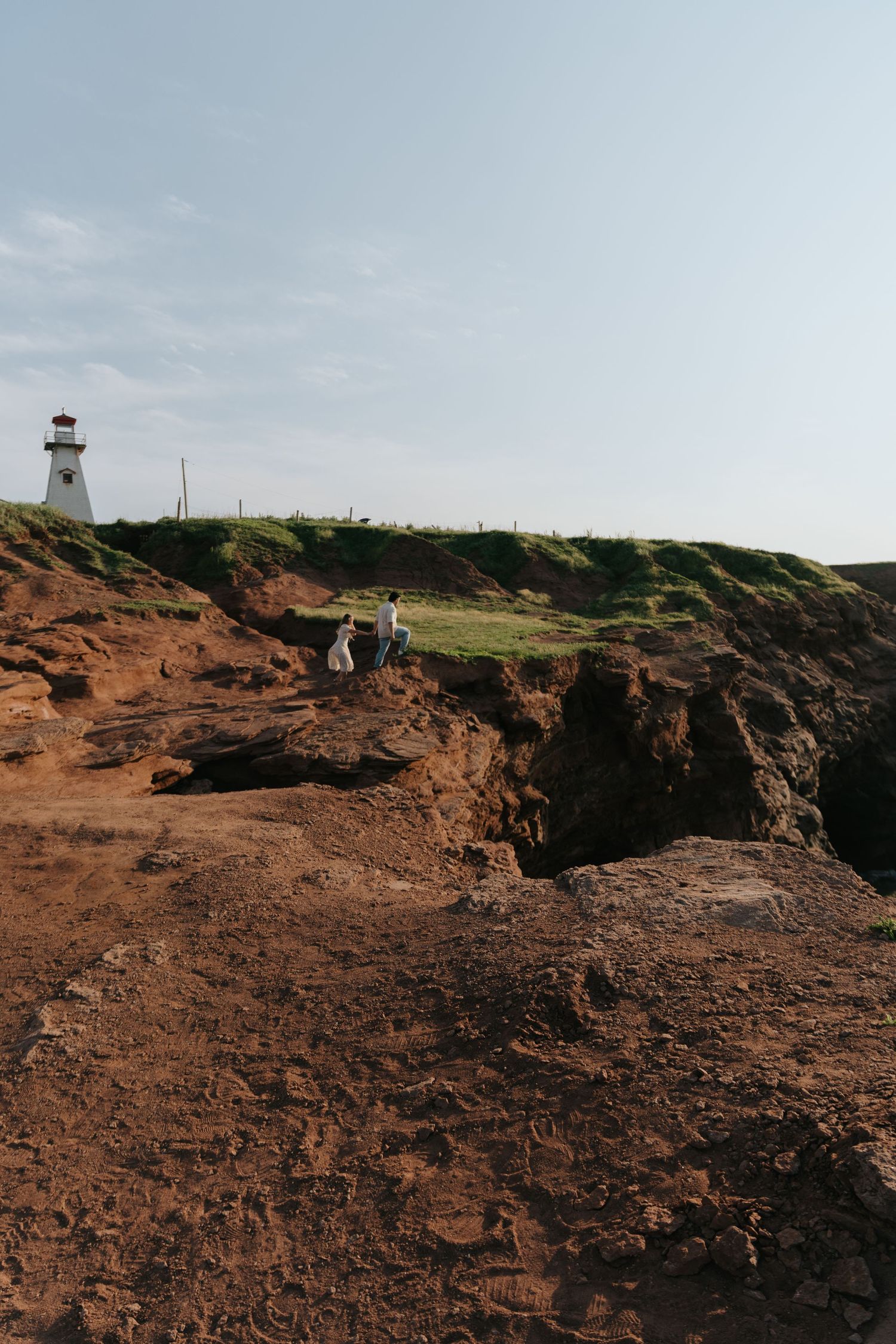 Rocky coastal cliffs with a lighthouse visible in the distance under cloudy skies.