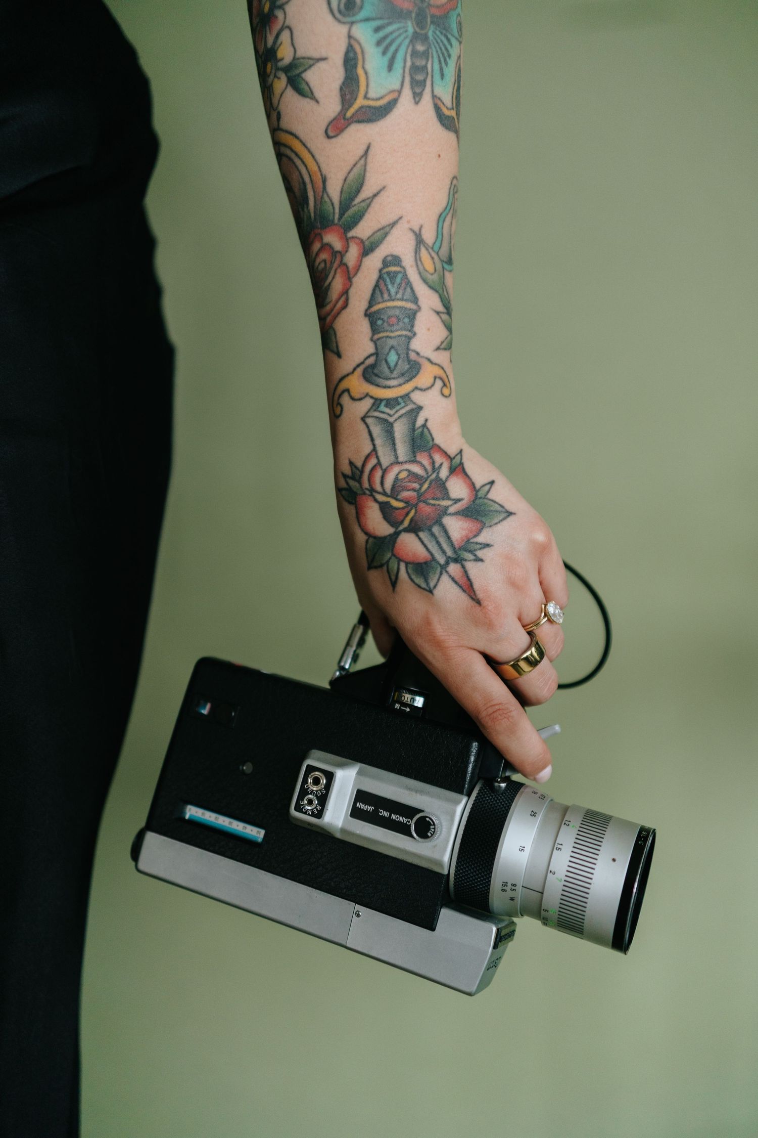 Tattooed arm holding a vintage camera against a green background.