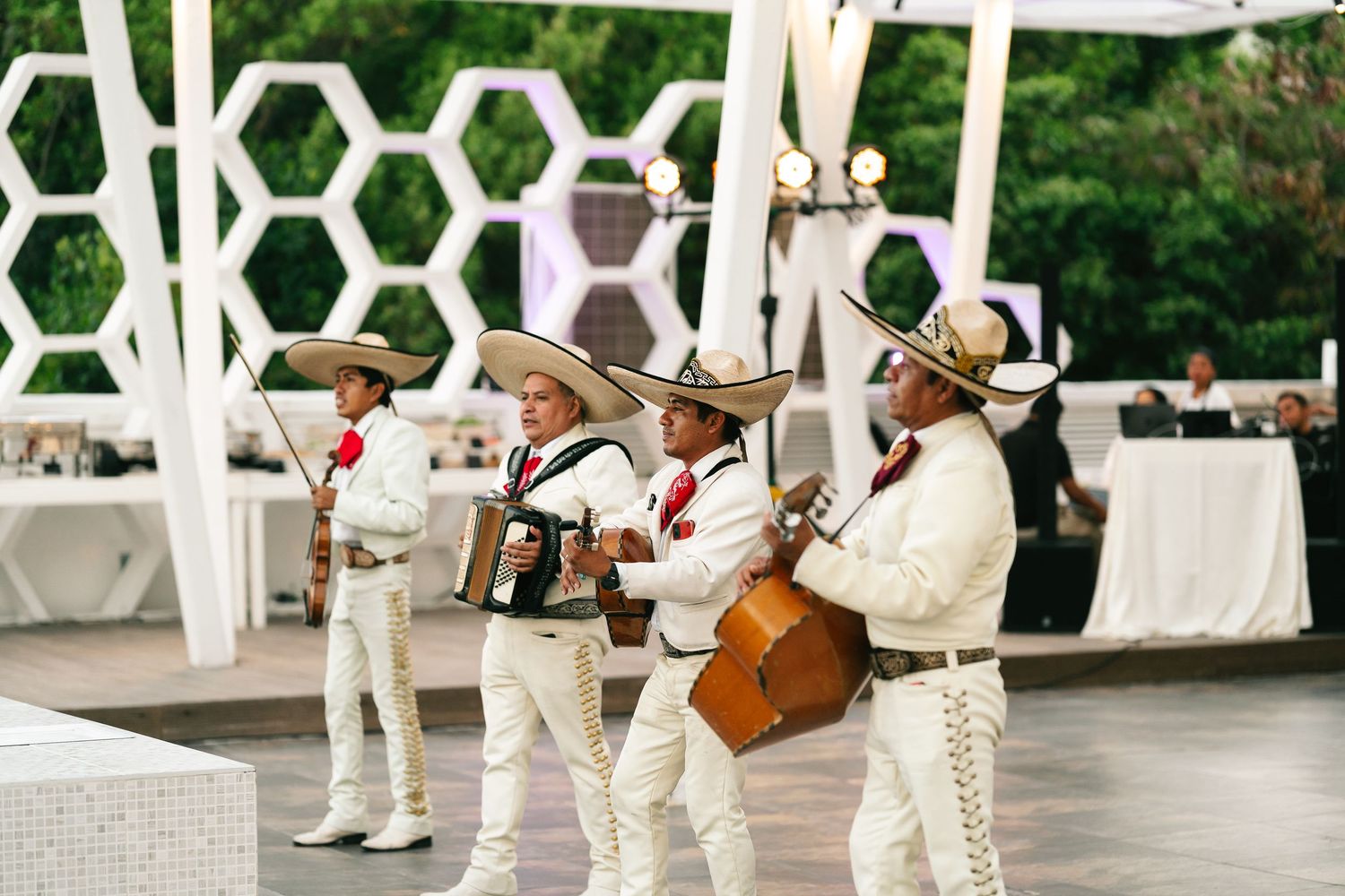Mariachi band in traditional white charro suits and sombreros performing at an outdoor event.