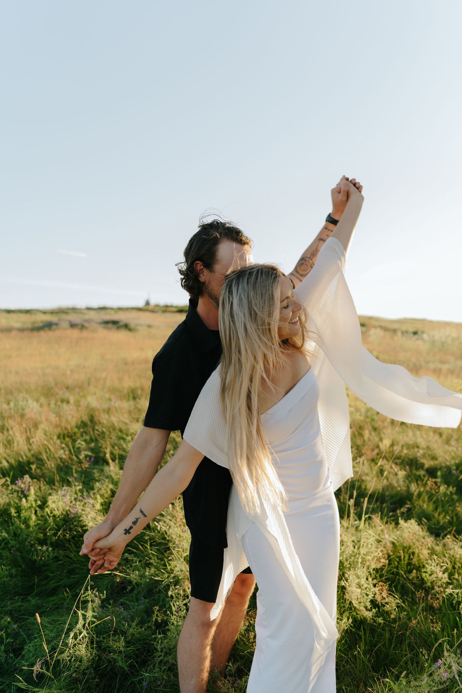 Couple in black and white outfits dancing playfully in a sunlit field.