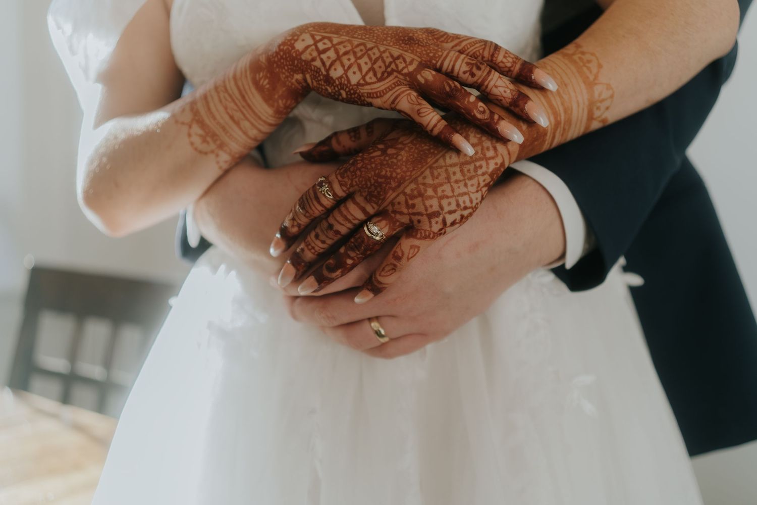 Close-up of intricate henna designs on hands with wedding rings.