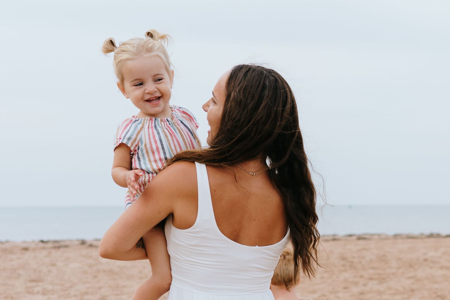 Joyful seaside interactions between adult and child in white and striped outfits.