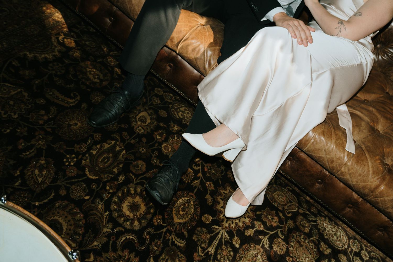 Detail shot of formal white dress and shoes against an ornate patterned carpet.