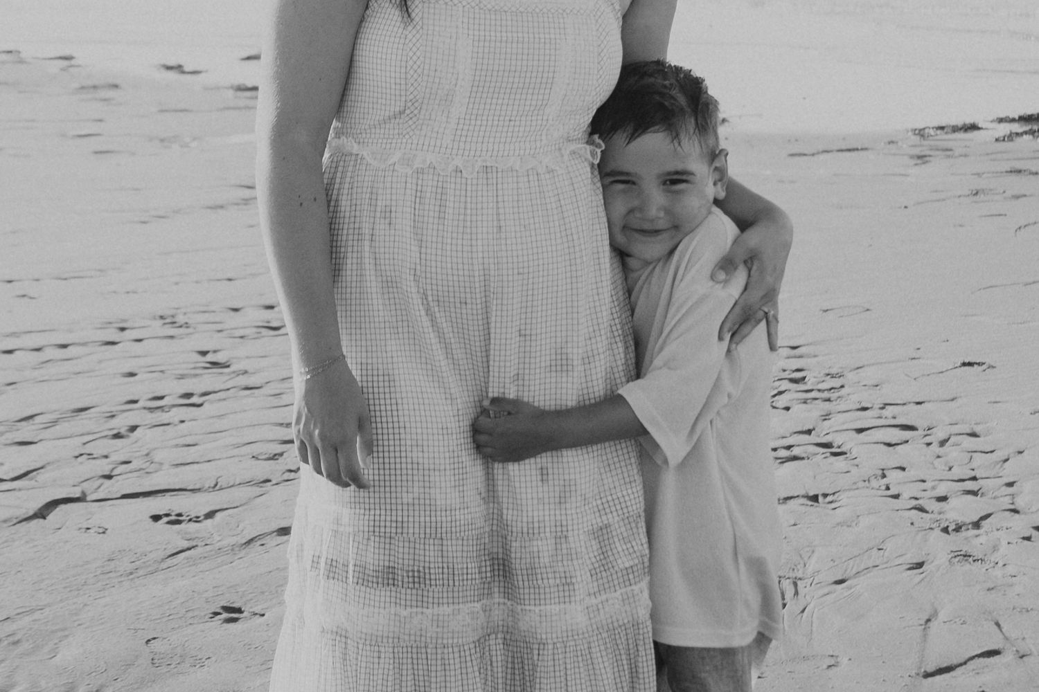 Black and white photo of a couple embracing on a beach during sunset.