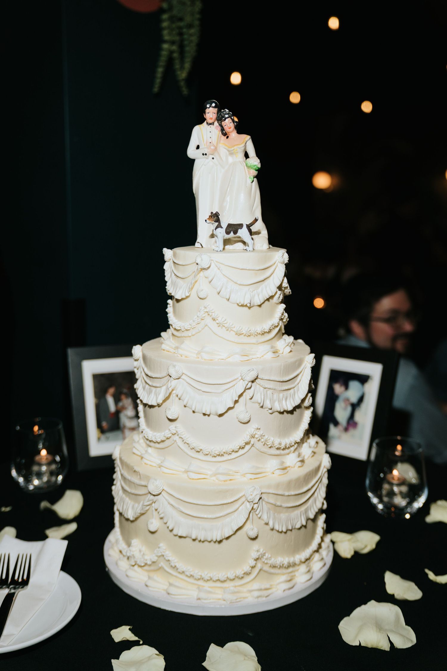 Elegant white tiered wedding cake with intricate piping details on dark background.