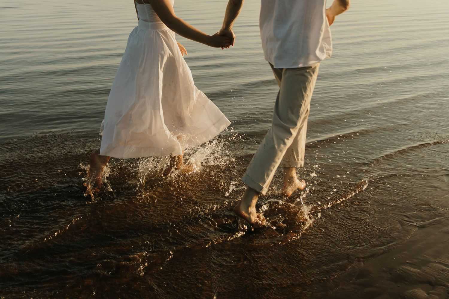 Couple splashing in water at sunset wearing wedding attire.