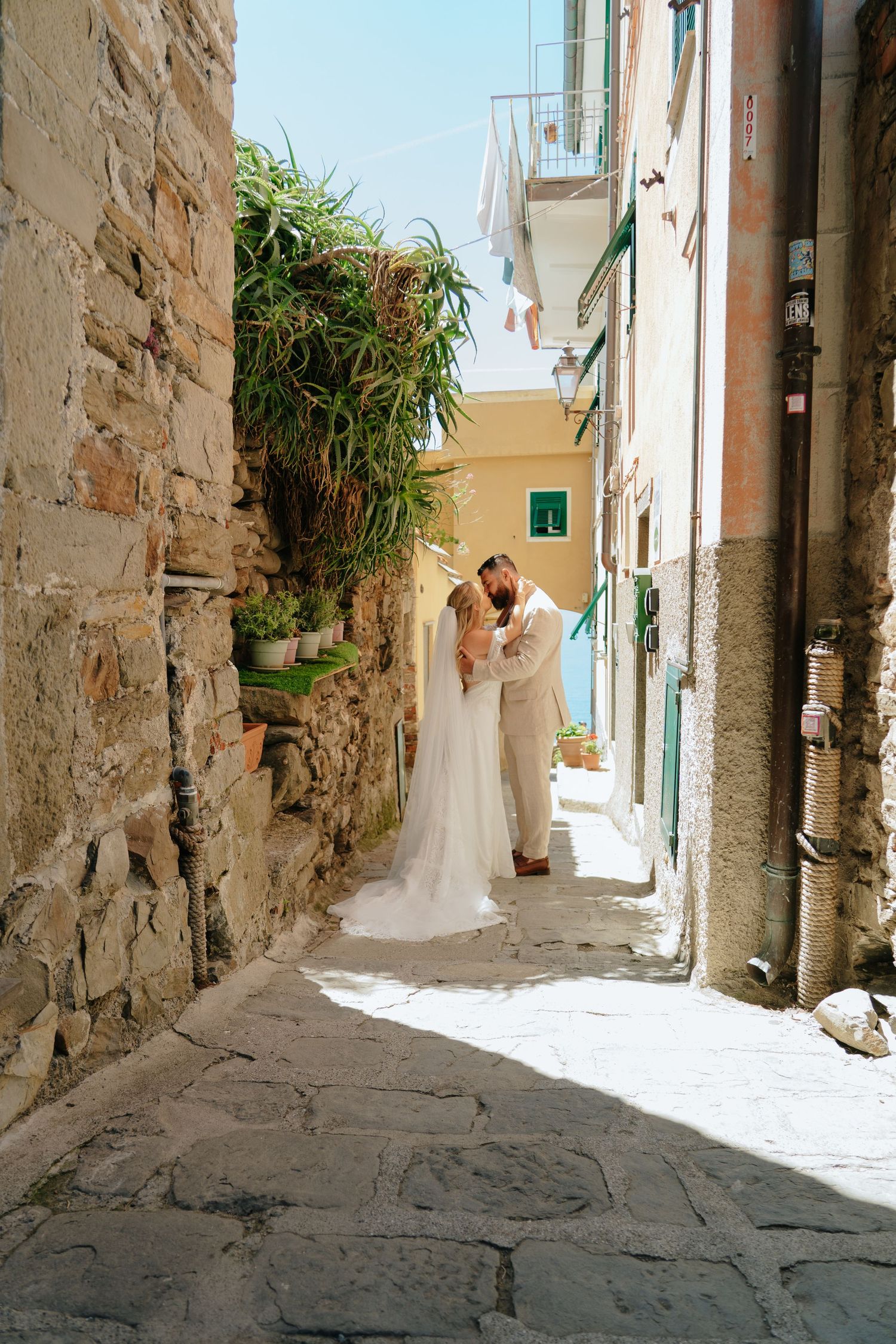 A couple in wedding attire shares an intimate moment in a narrow Italian alleyway.