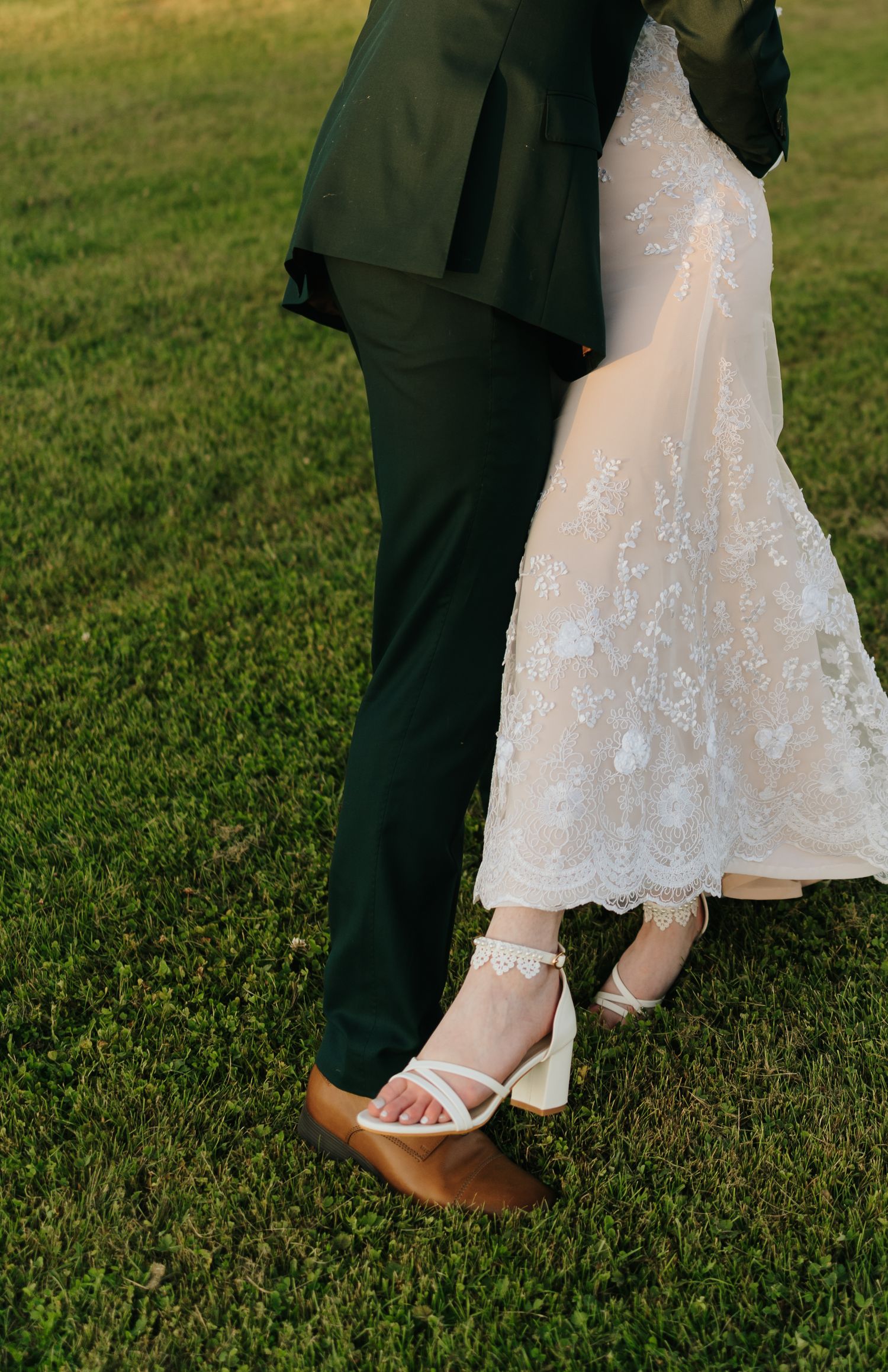 Close-up of bride and groom's feet on grass, showing wedding shoes and dress hem.