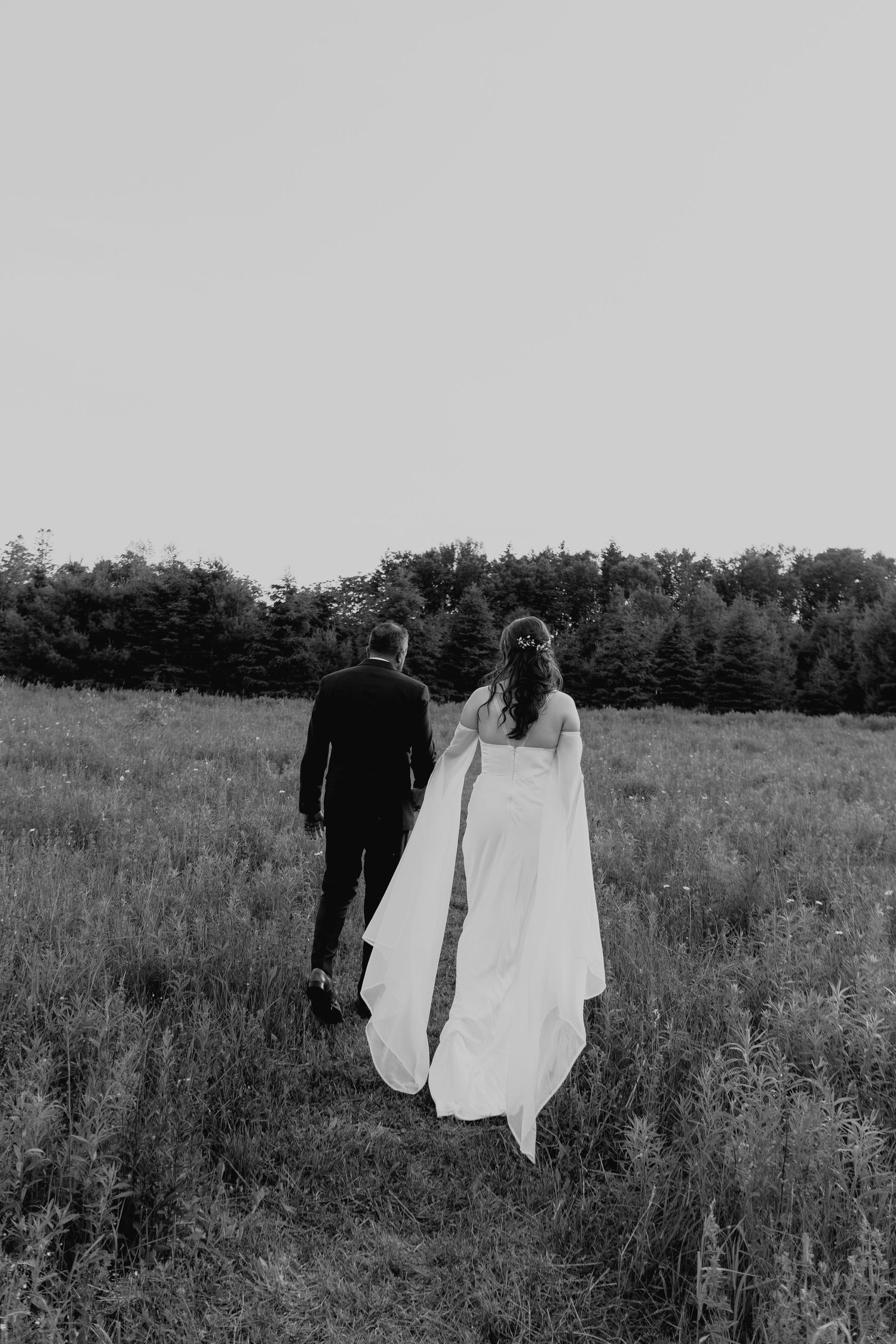 A couple walks away through a wildflower field in black and white.
